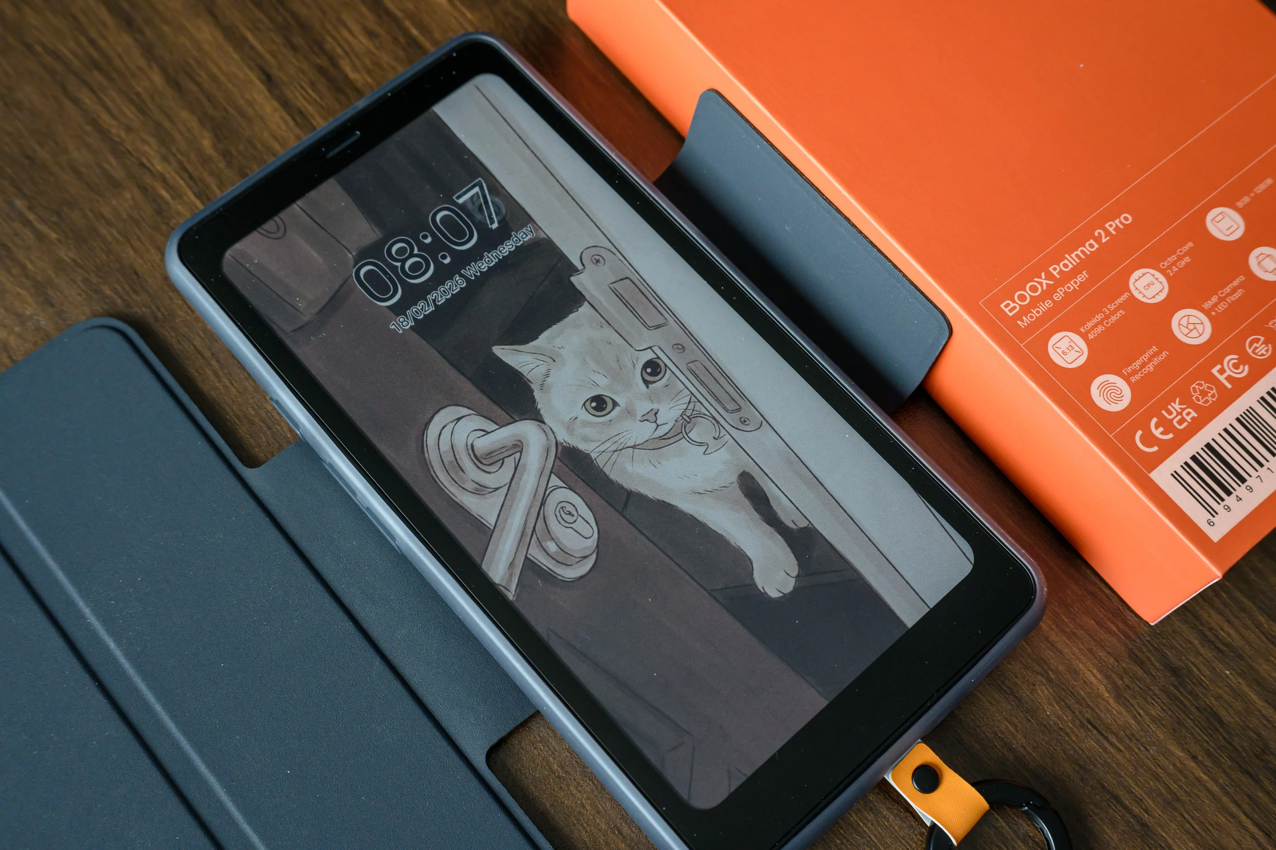 A phone-sized e-reader in a blue folio case beside its orange box on a wooden table