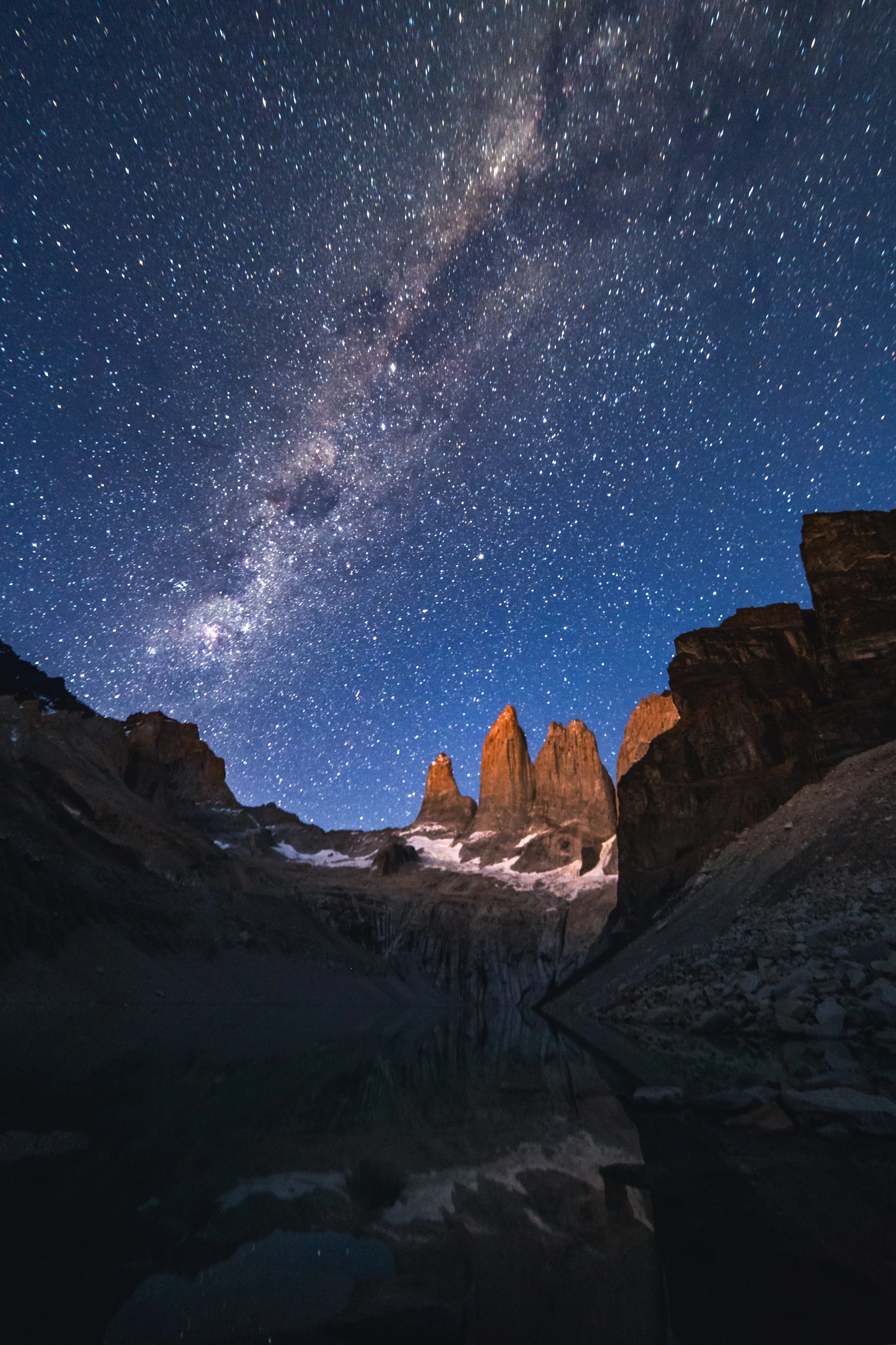 The Milky Way above granite towers glowing in first light over a mountain lake