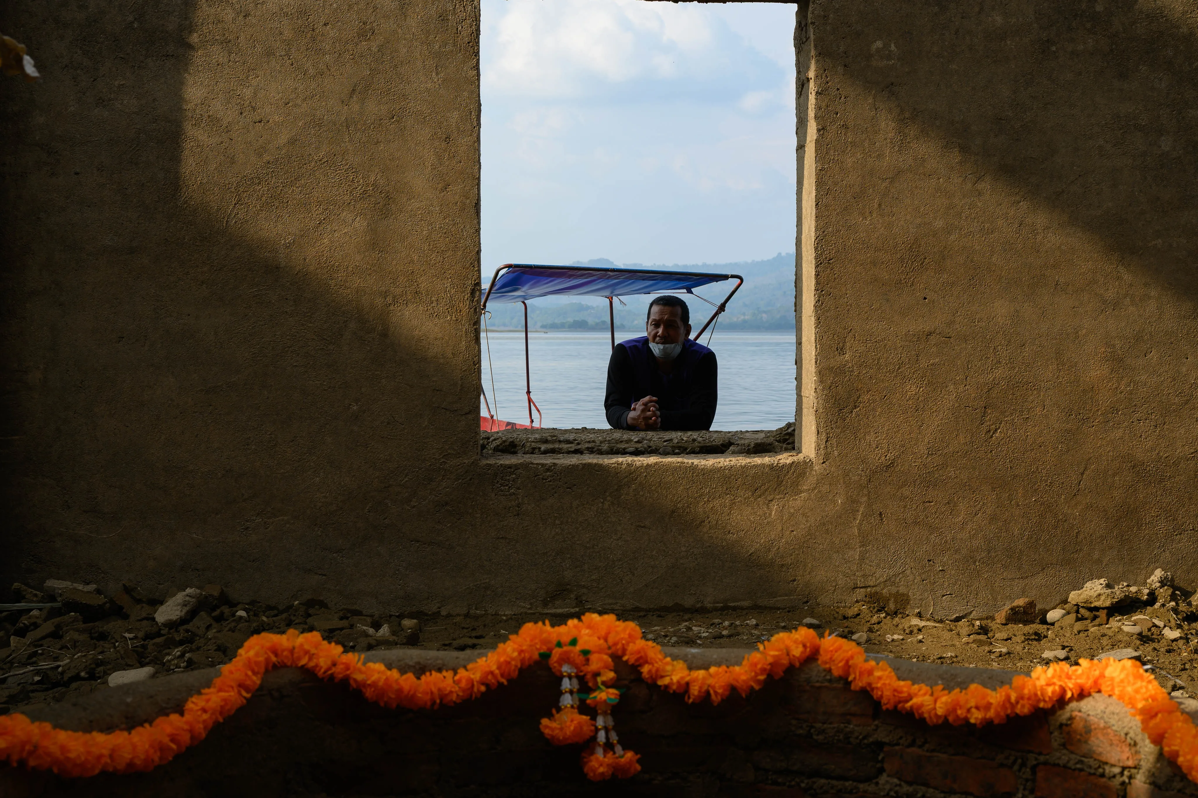 A man framed in a window above a string of marigold flowers