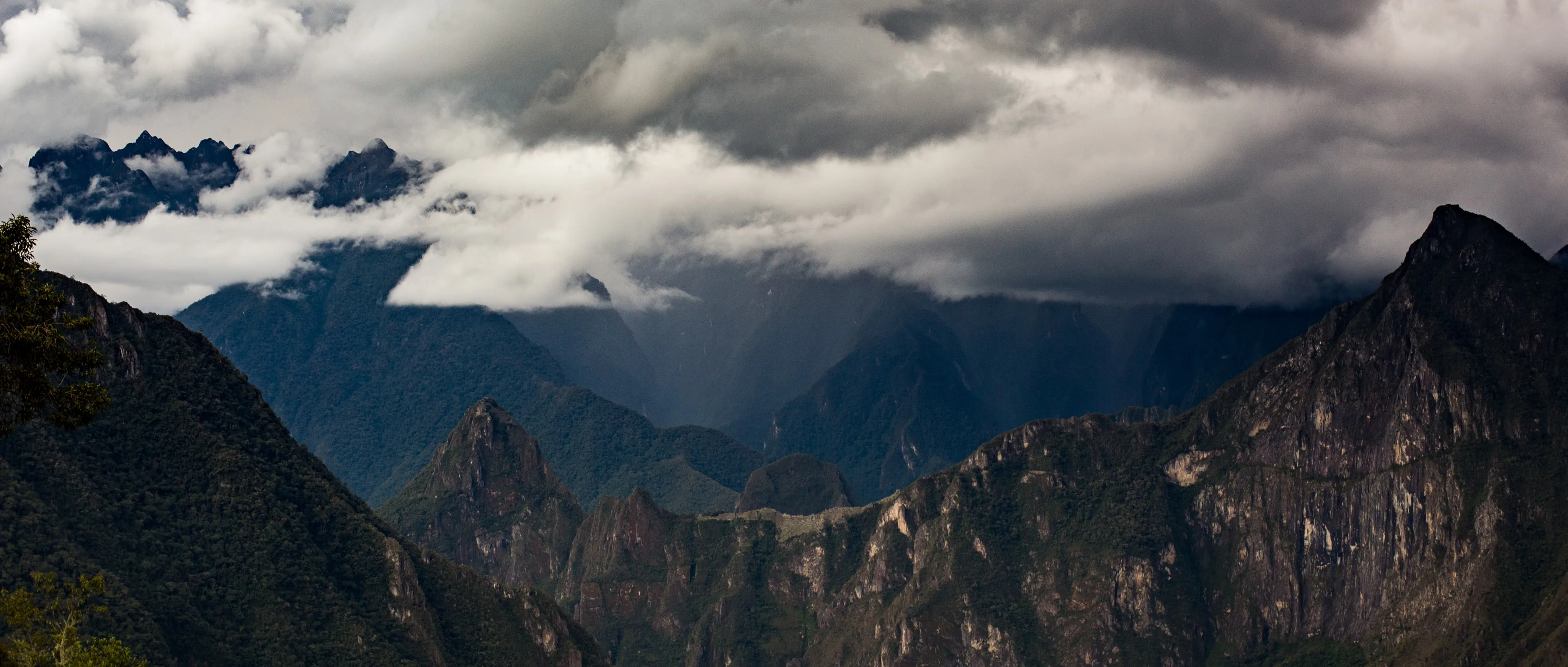 A telephoto view of Machu Picchu's ruined terraces and peaks under storm clouds, the ridgeline said to resemble a condor in flight.