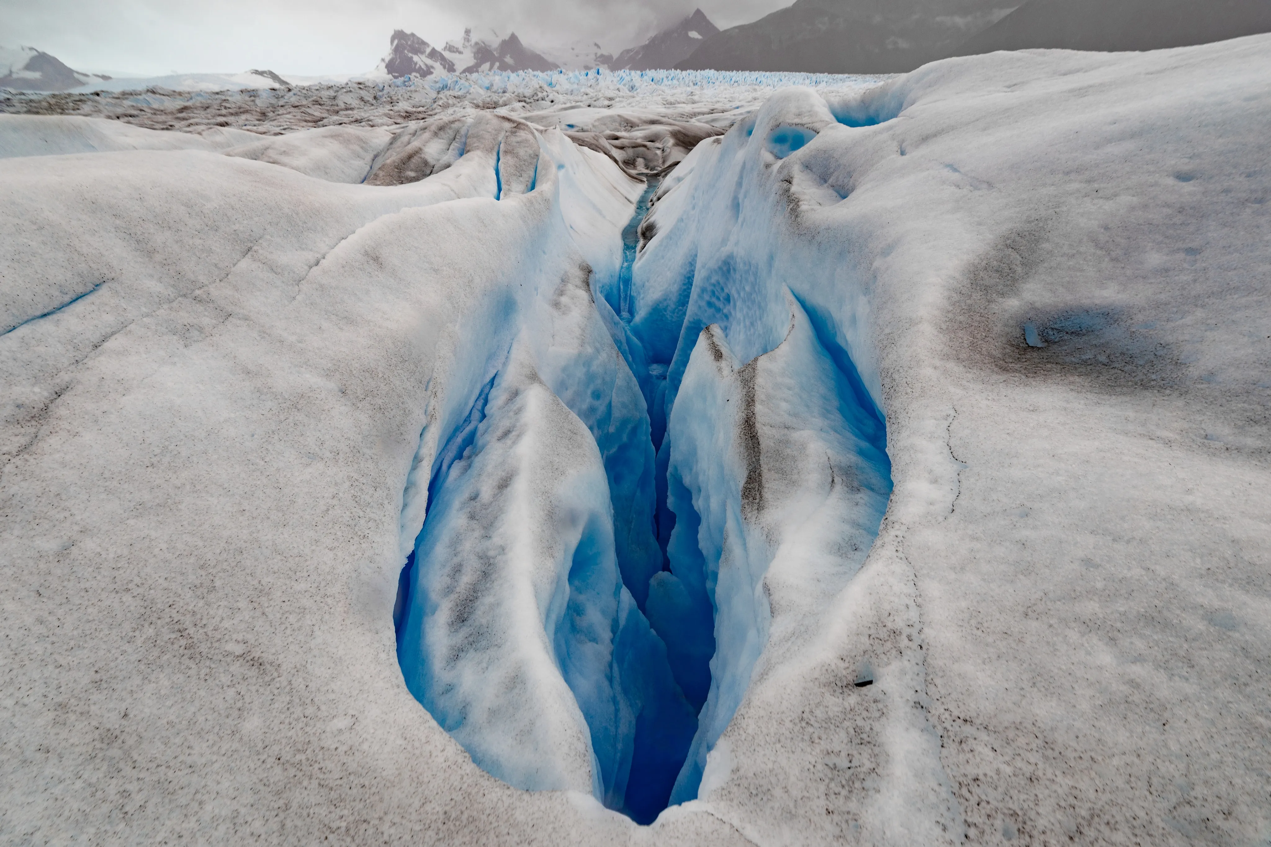 A deep blue glacial crevasse with meltwater flowing through the ice