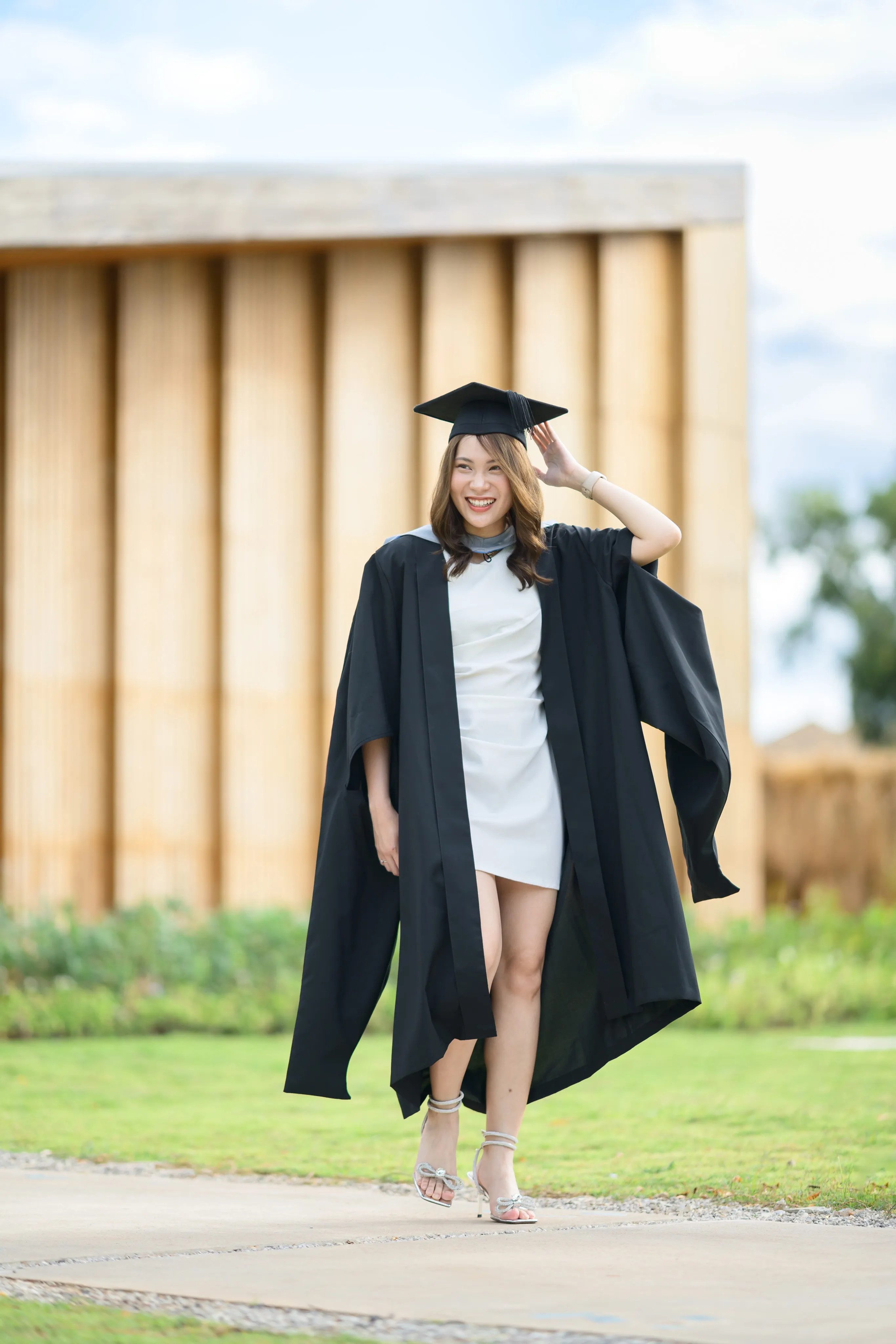 A graduate adjusting her cap and smiling outdoors
