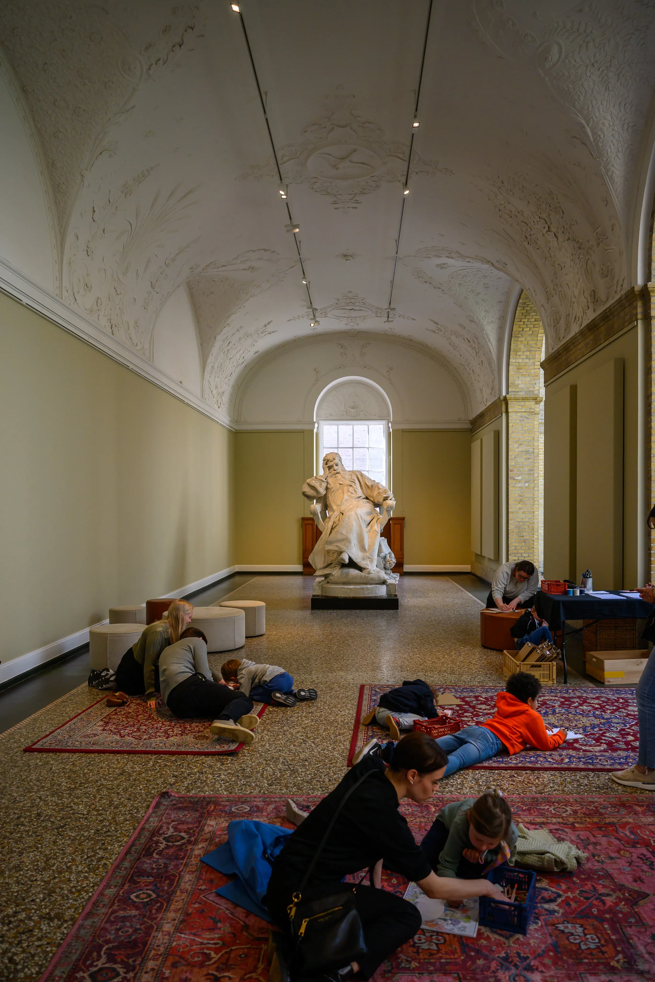 Visitors resting on the floor beside a statue in a museum hall