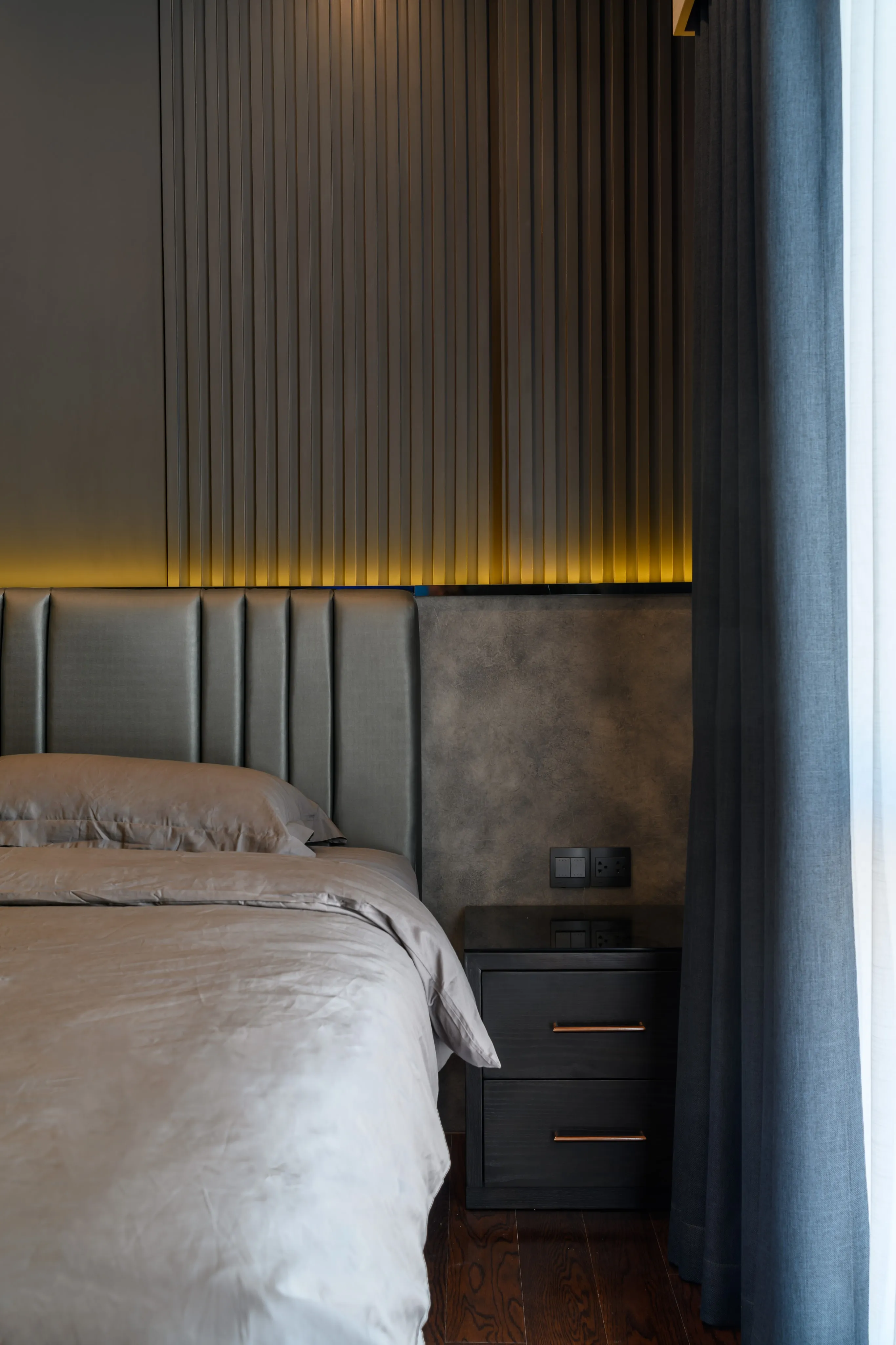 Photograph matching a dark modern bedroom design with a close view of the bed and bedside lamp