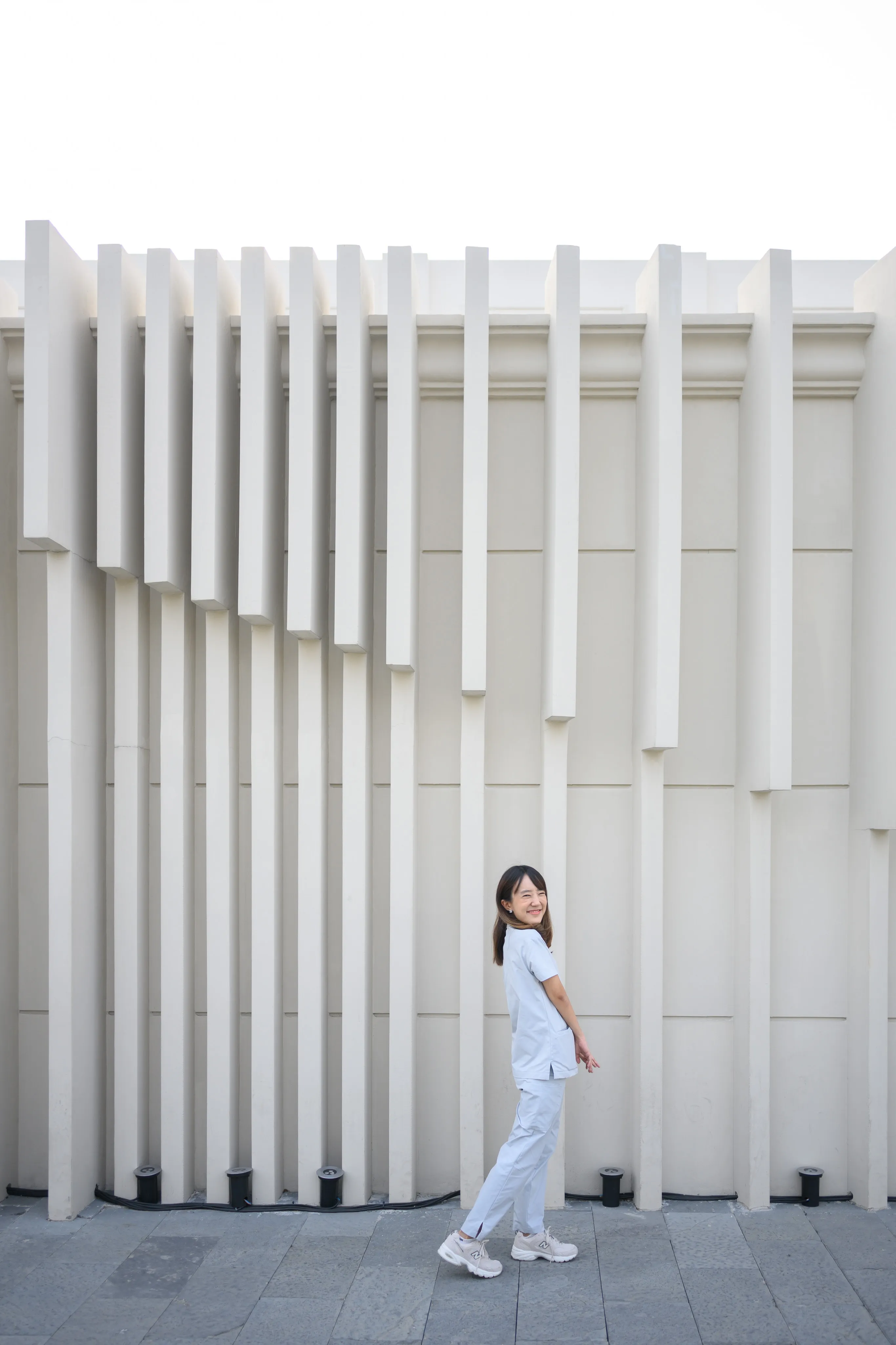 A woman standing against a fluted white architectural facade.