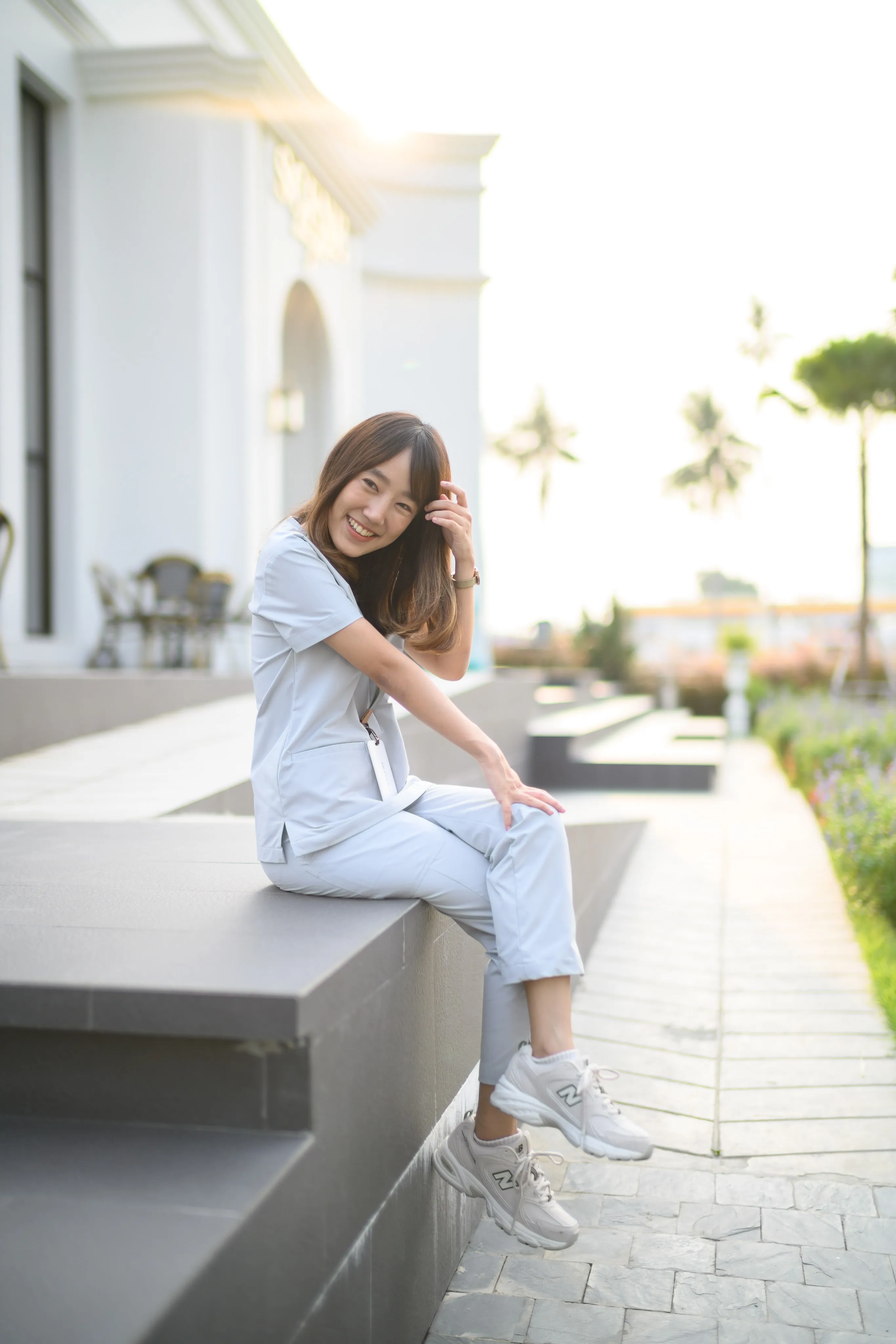 A woman sitting on a stone ledge in a palm-lined courtyard.