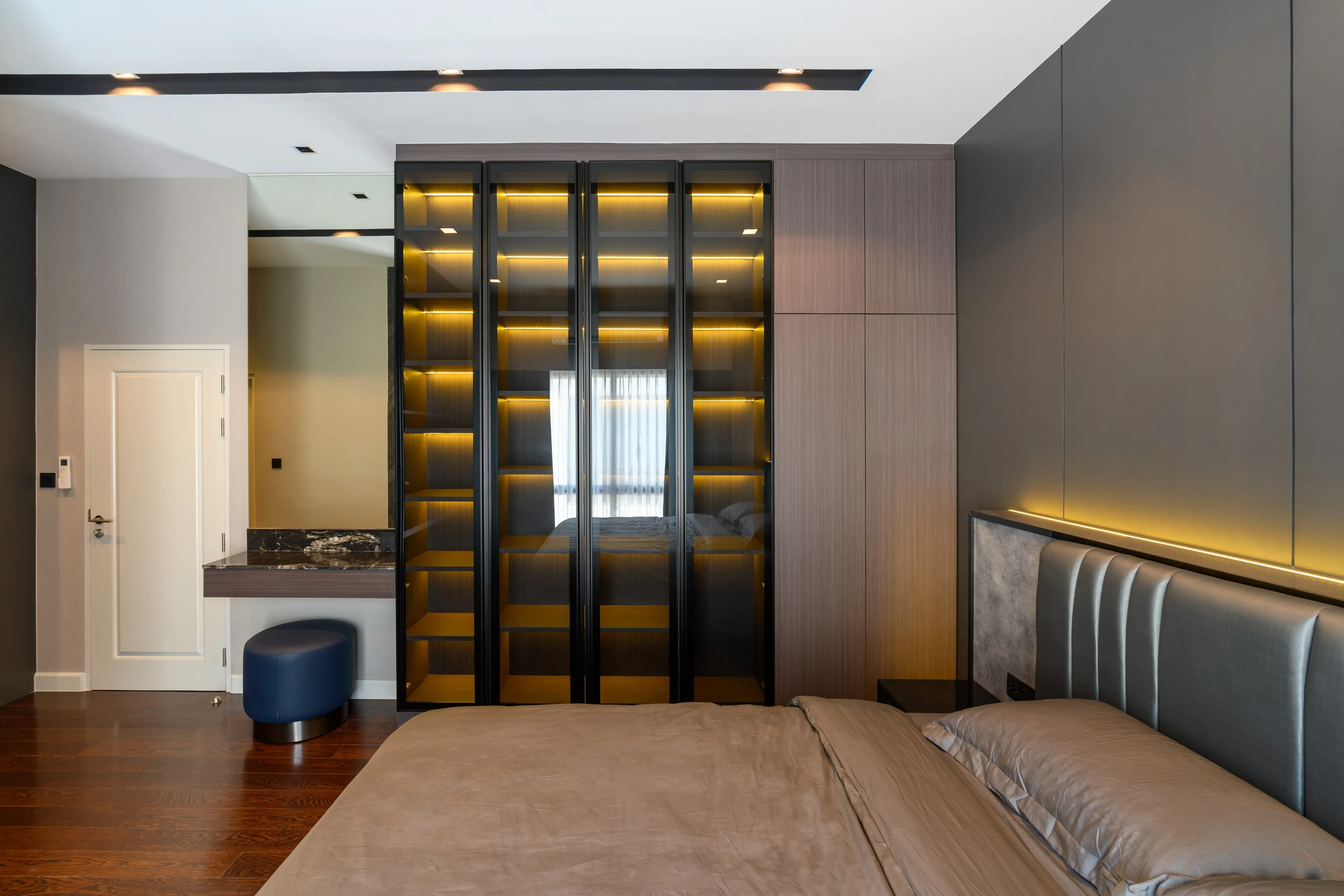 Photograph of a modern bedroom facing illuminated shelving and a marble accent wall