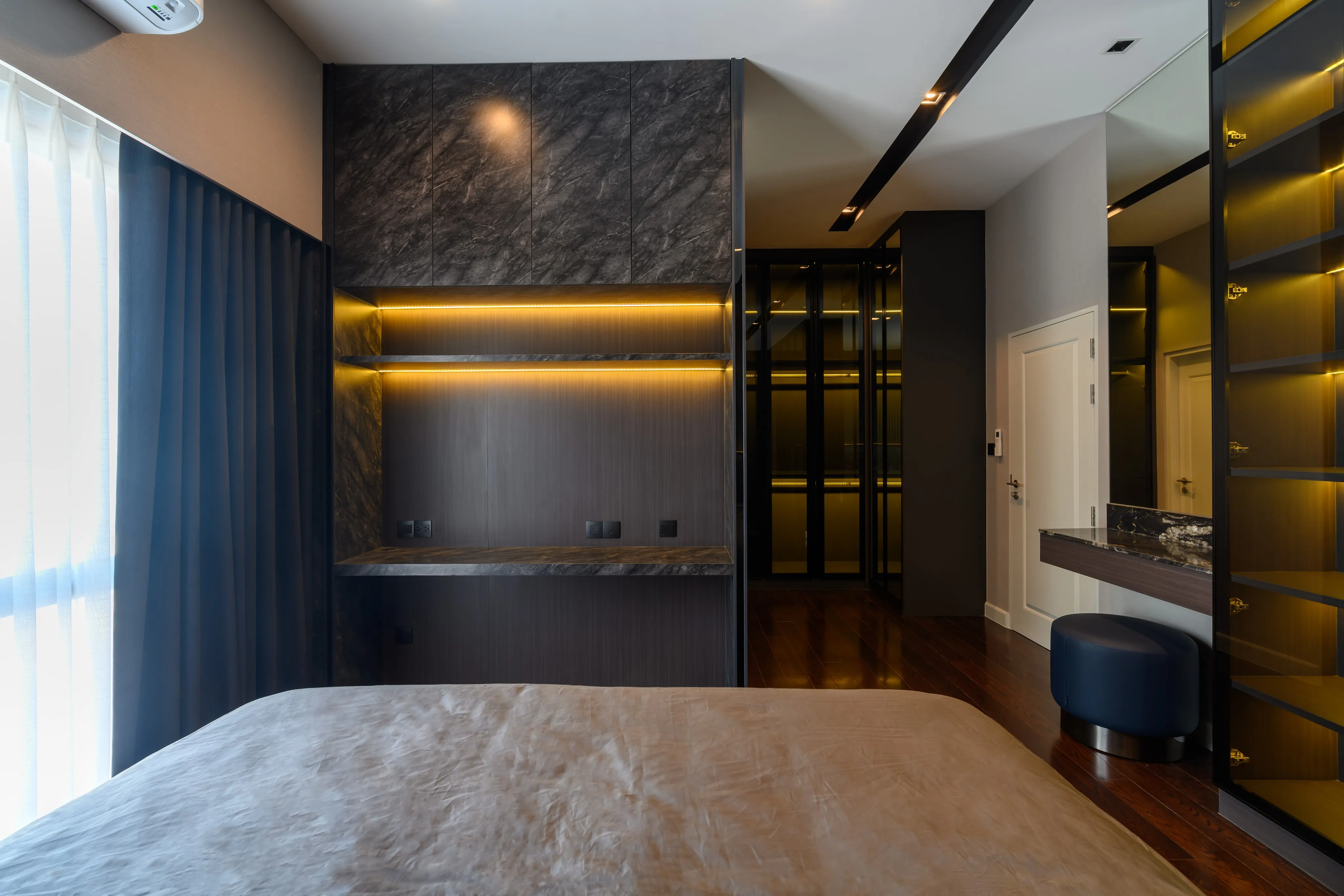 Photograph of a modern bedroom with a desk, illuminated shelving, and wardrobe