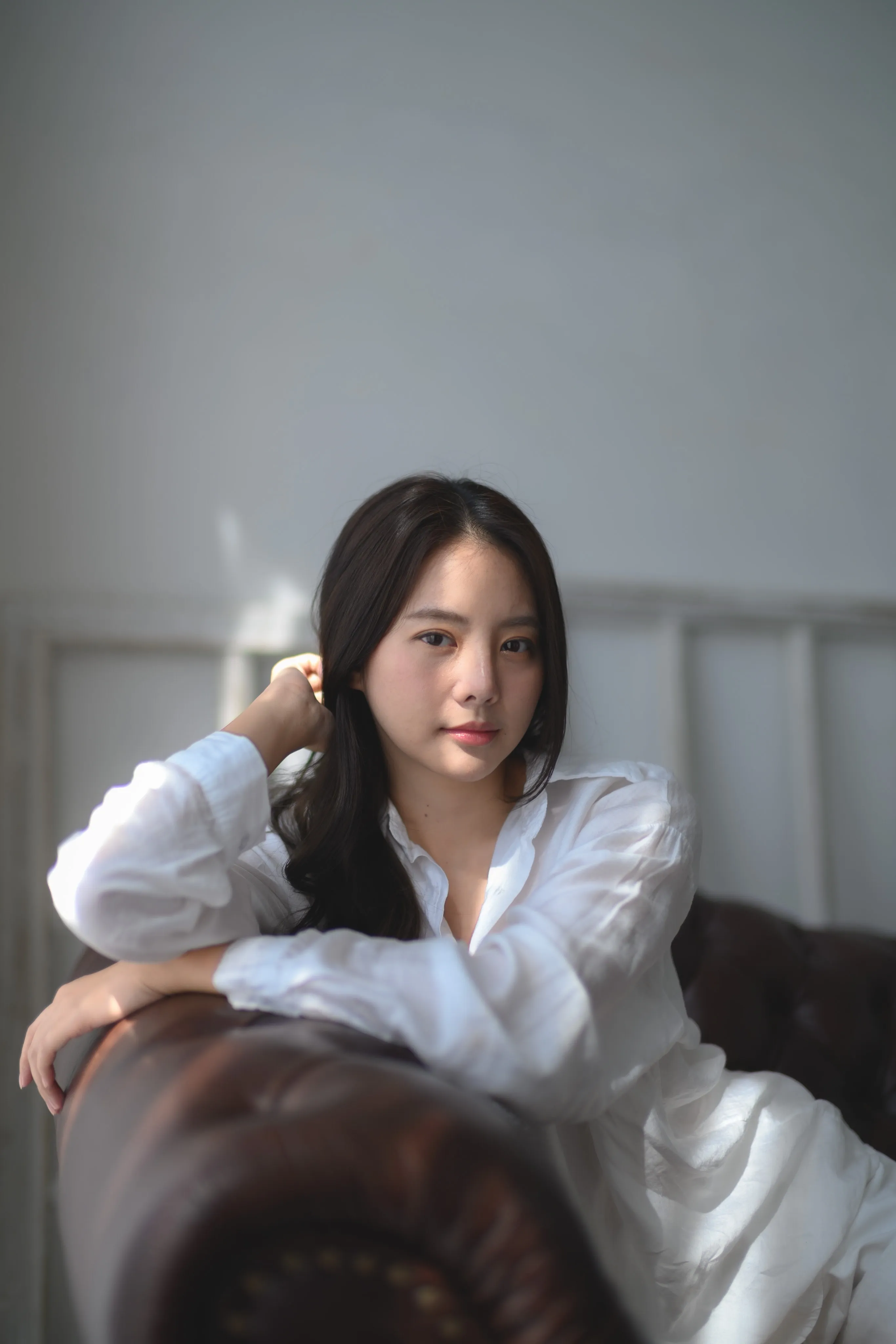 A woman in a white shirt leaning on a leather armchair, smiling.