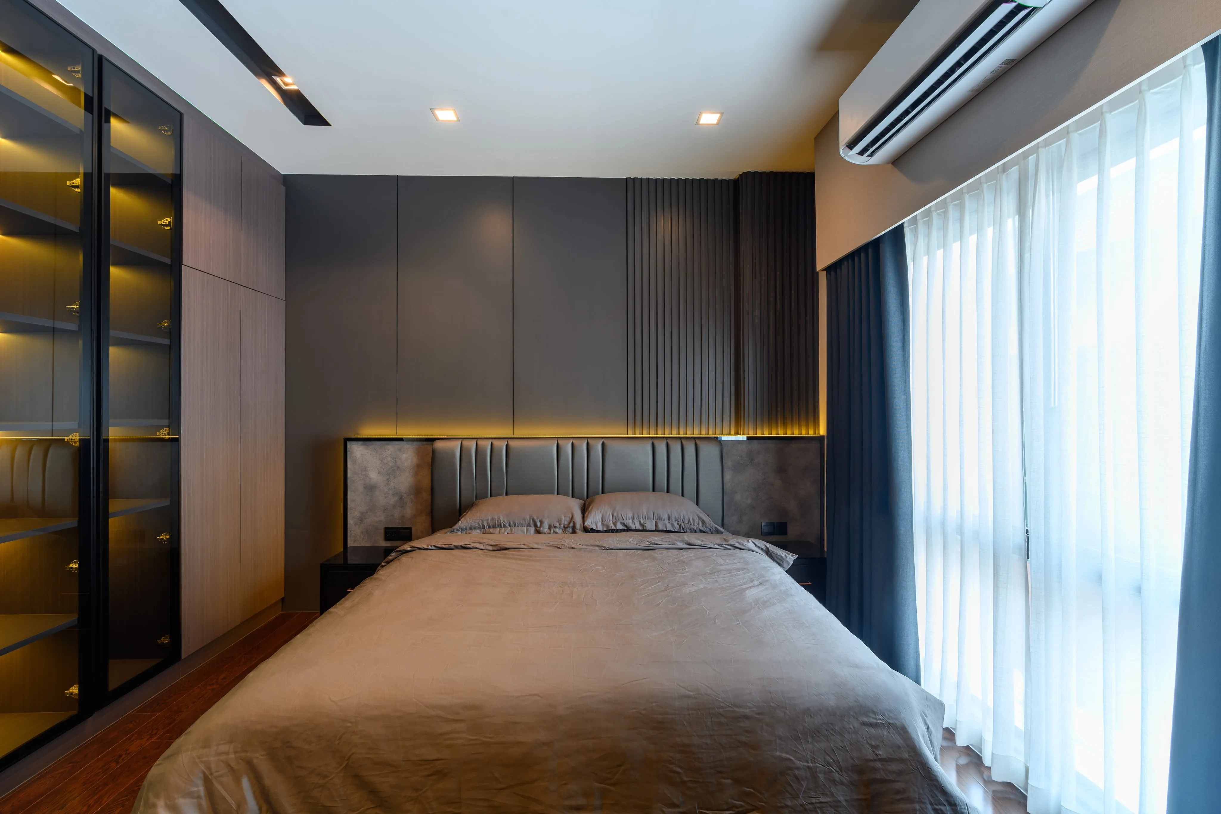 Photograph of a gray bedroom viewed from the foot of the bed beside a large window