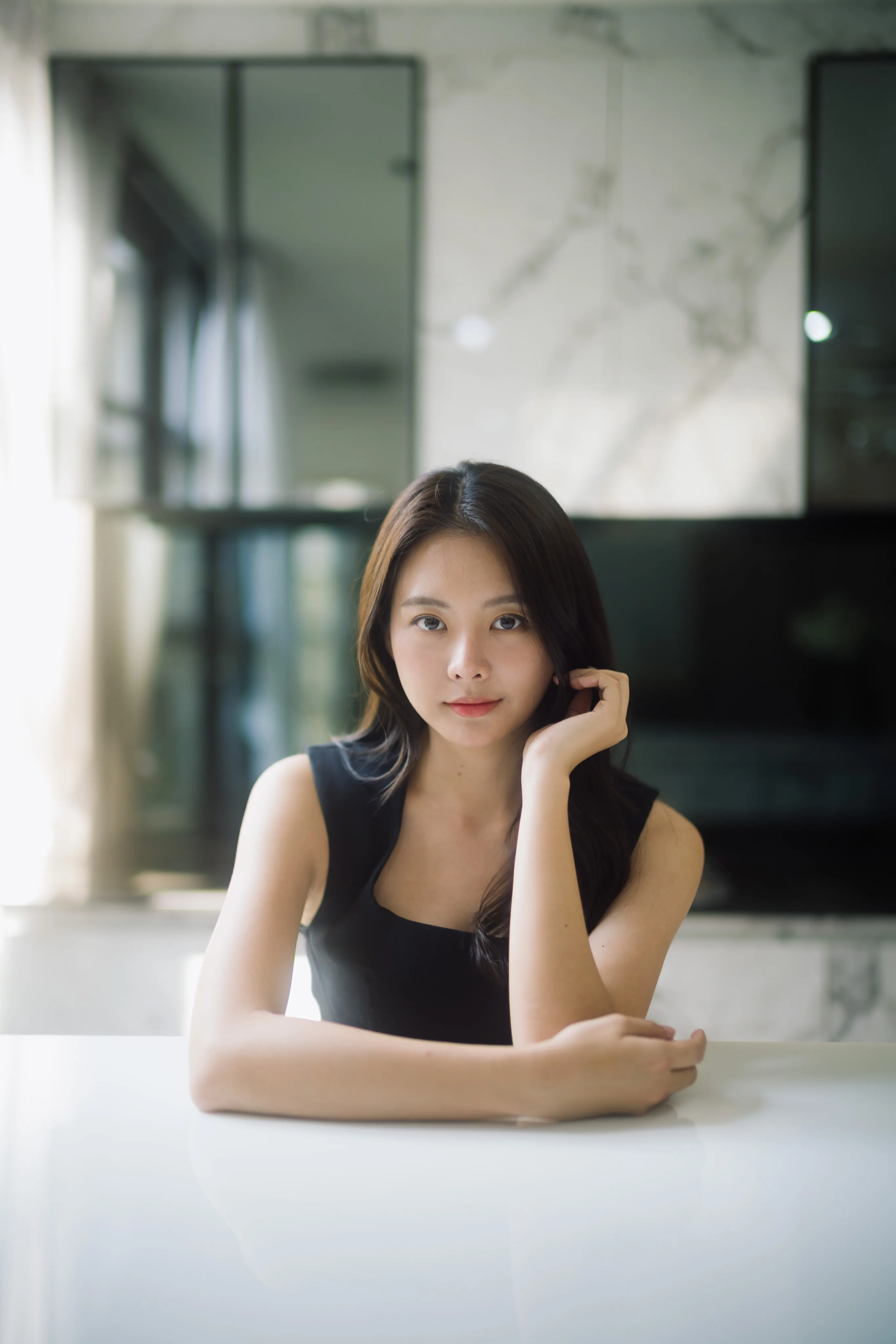 A woman in a black dress resting her chin on her hand at a white table.