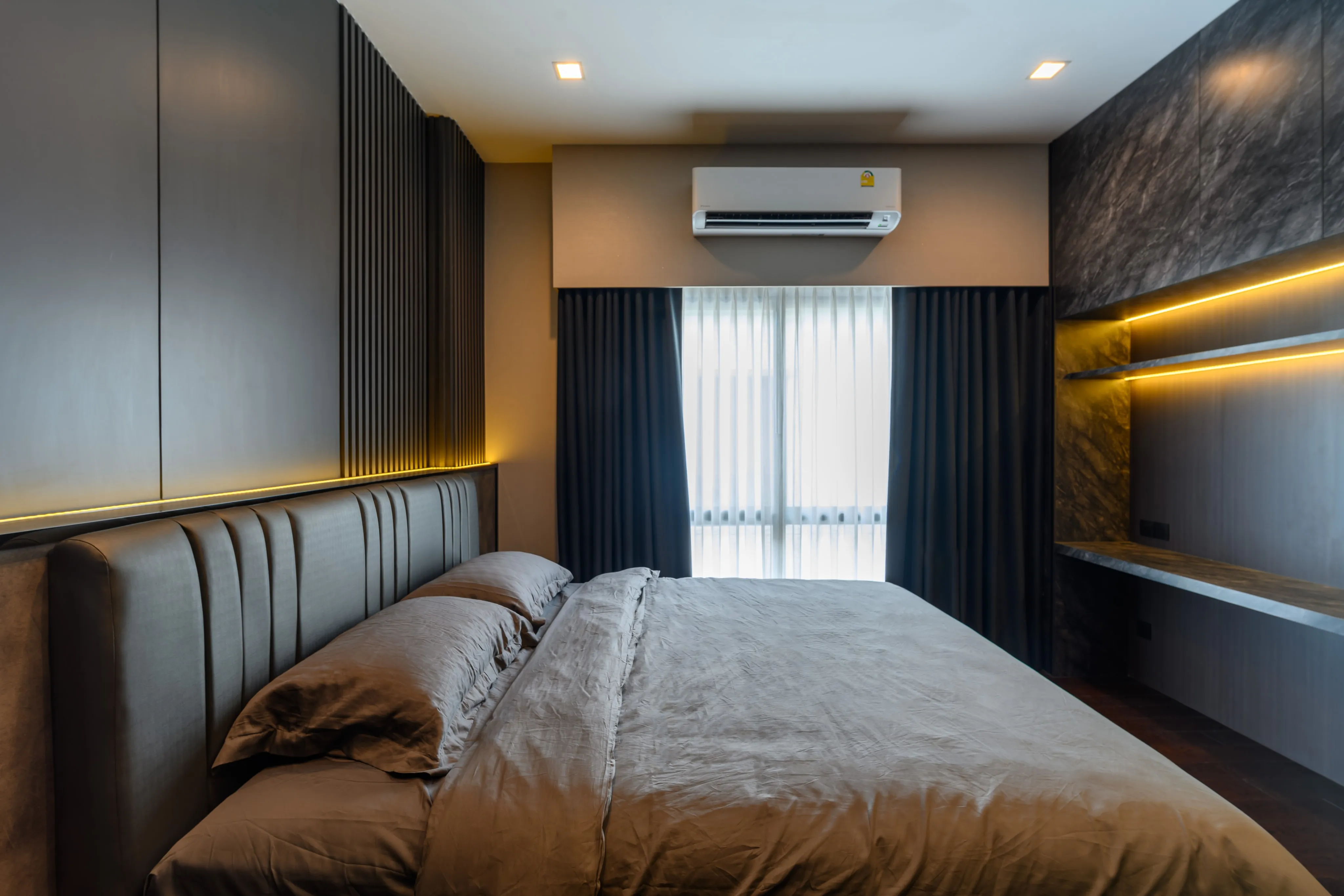 Photograph of a compact bedroom with a padded wall, television wall, and curtained window