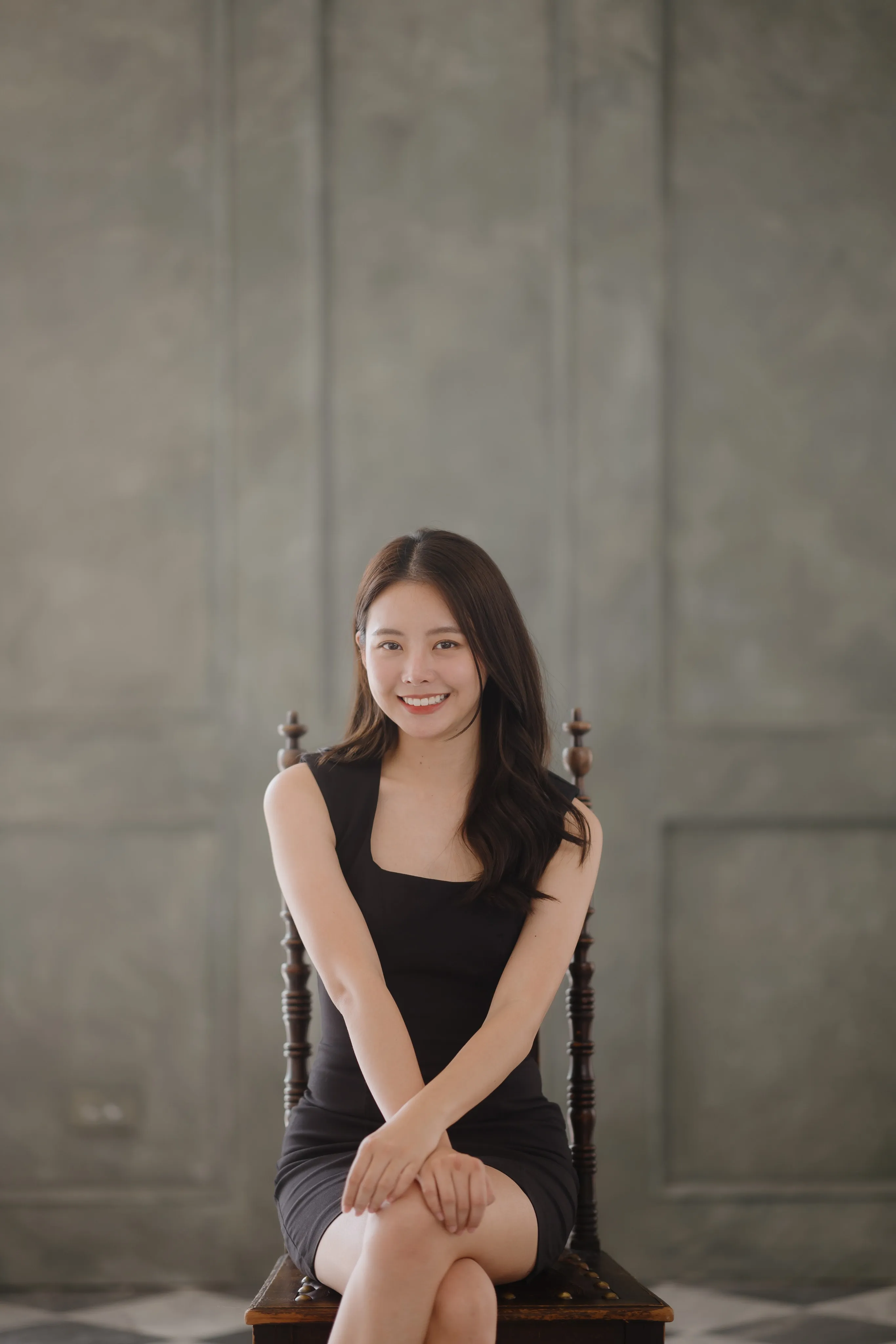 A woman in a black dress sitting on a carved wooden chair, smiling.