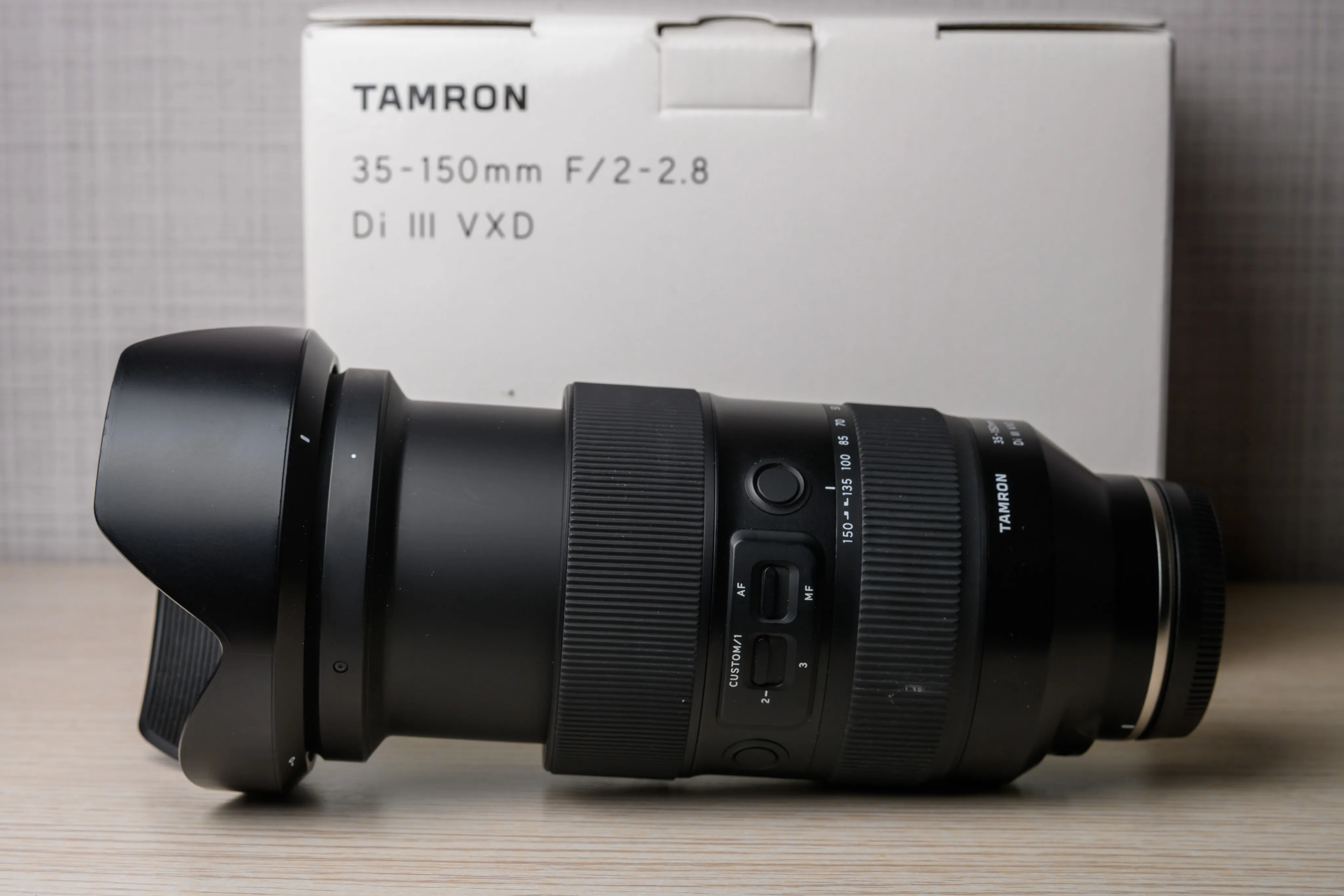 A zoom lens resting sideways beside its packaging