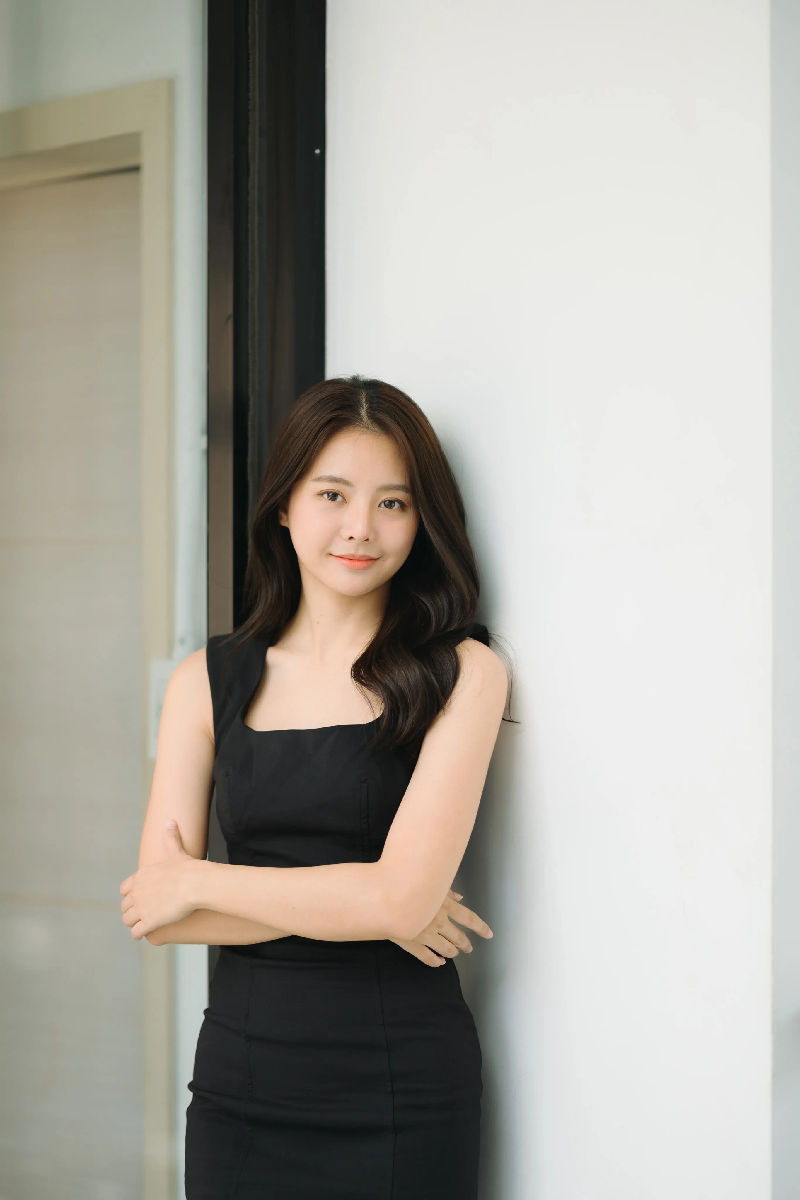 A woman in a black dress leaning against a doorway with arms crossed.