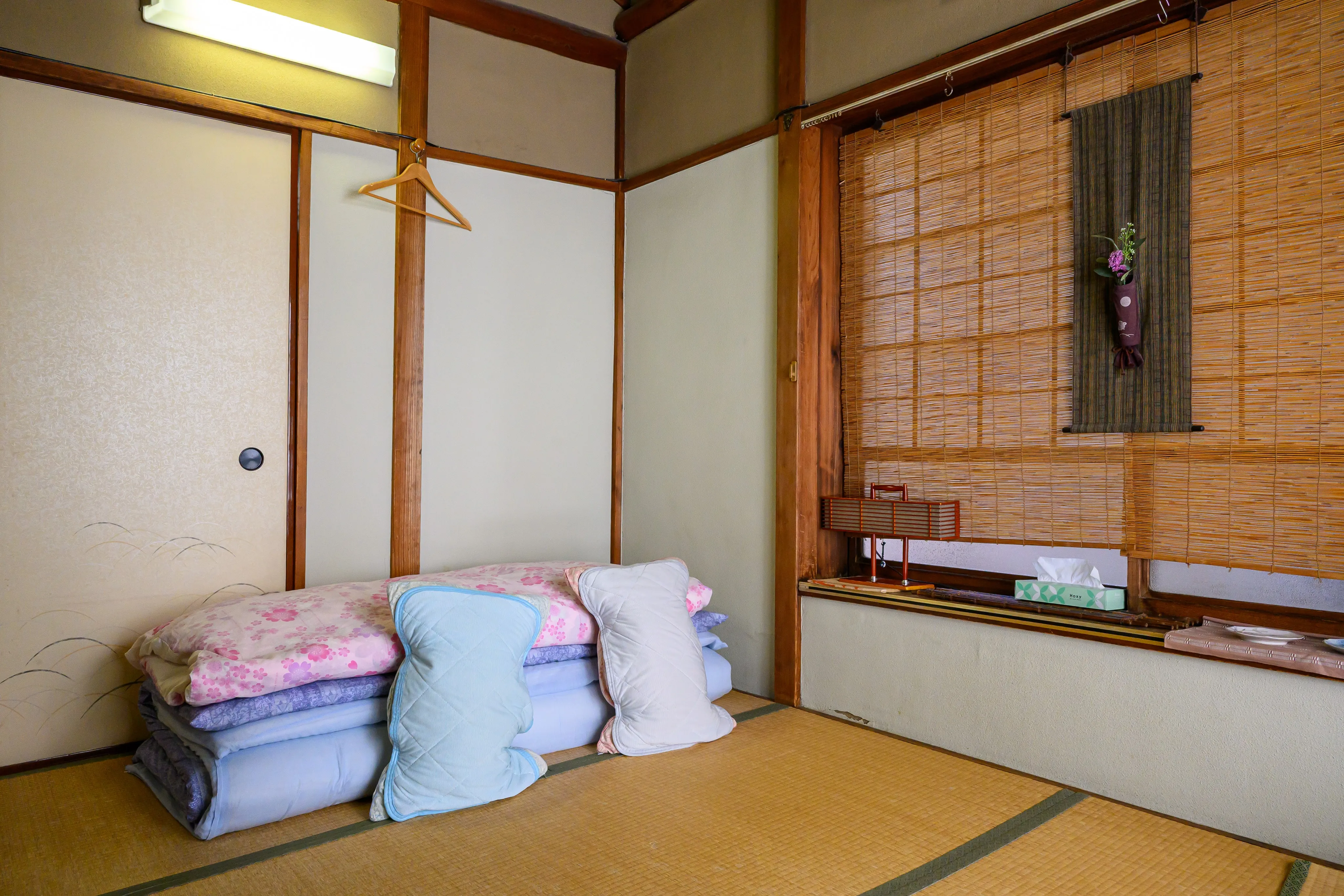 Corner of a traditional tatami room with folded bedding and pastel cushions