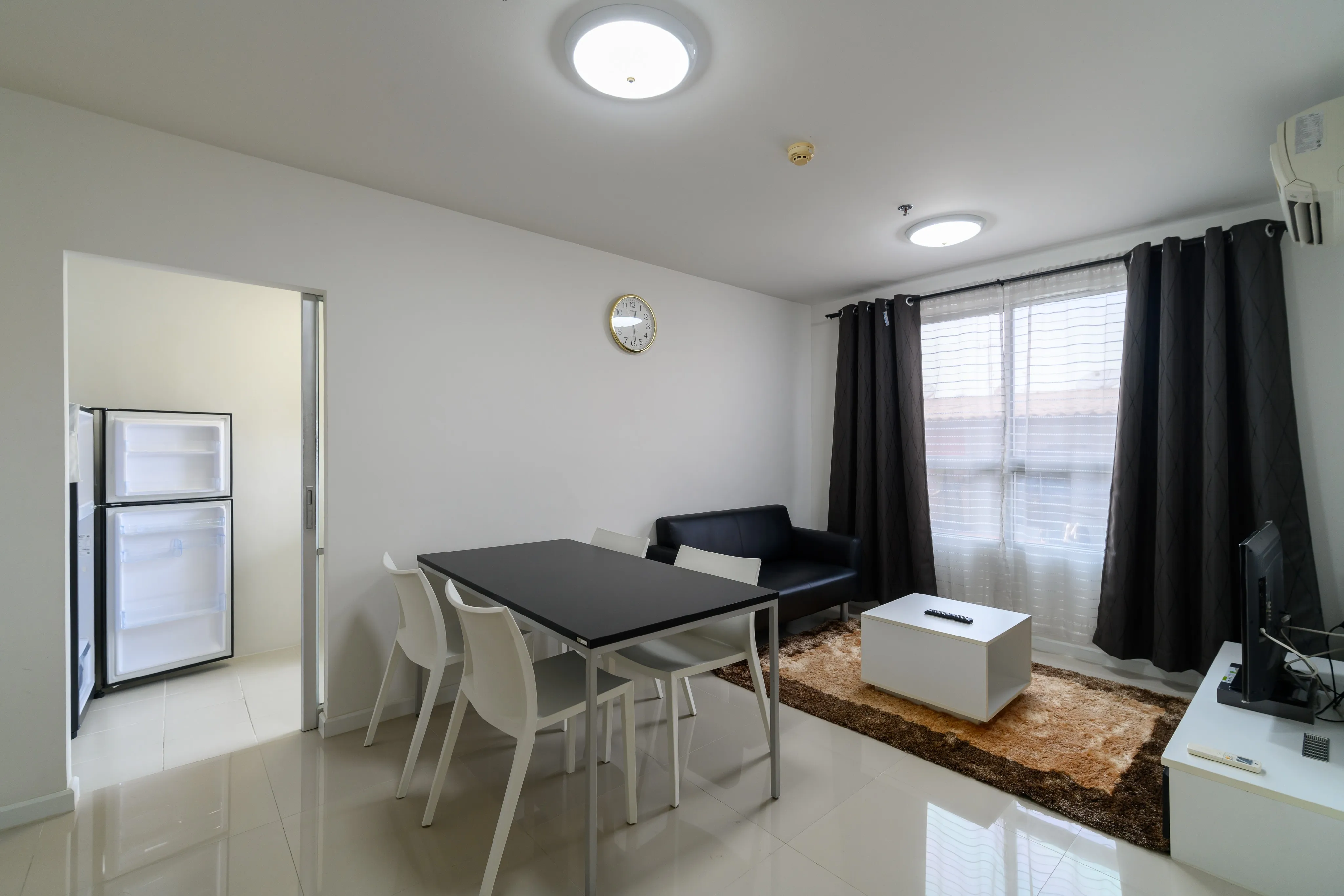 Bright apartment living and dining area with white chairs and dark curtains