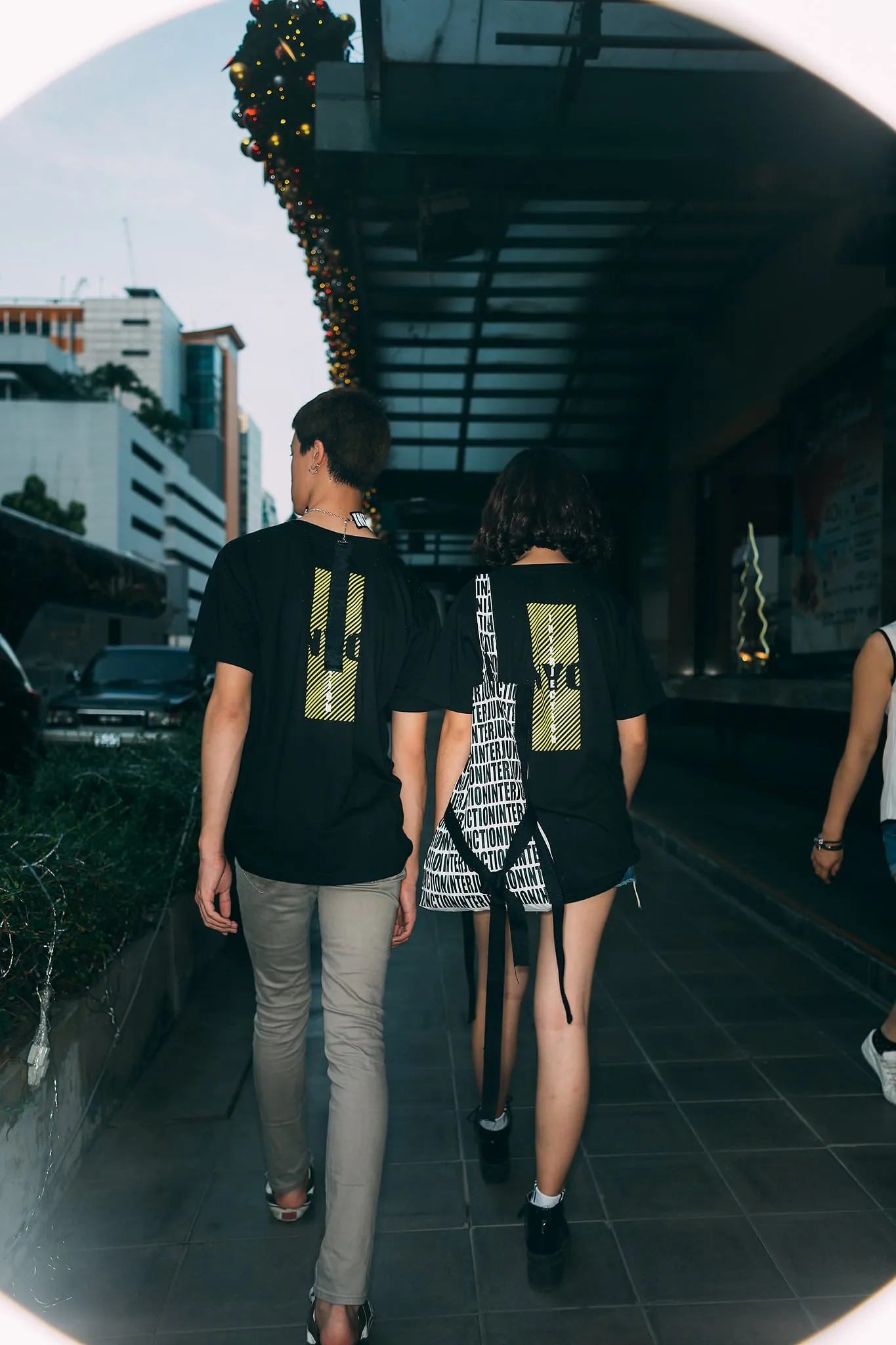 Two people in black graphic T-shirts walking away down a covered city sidewalk