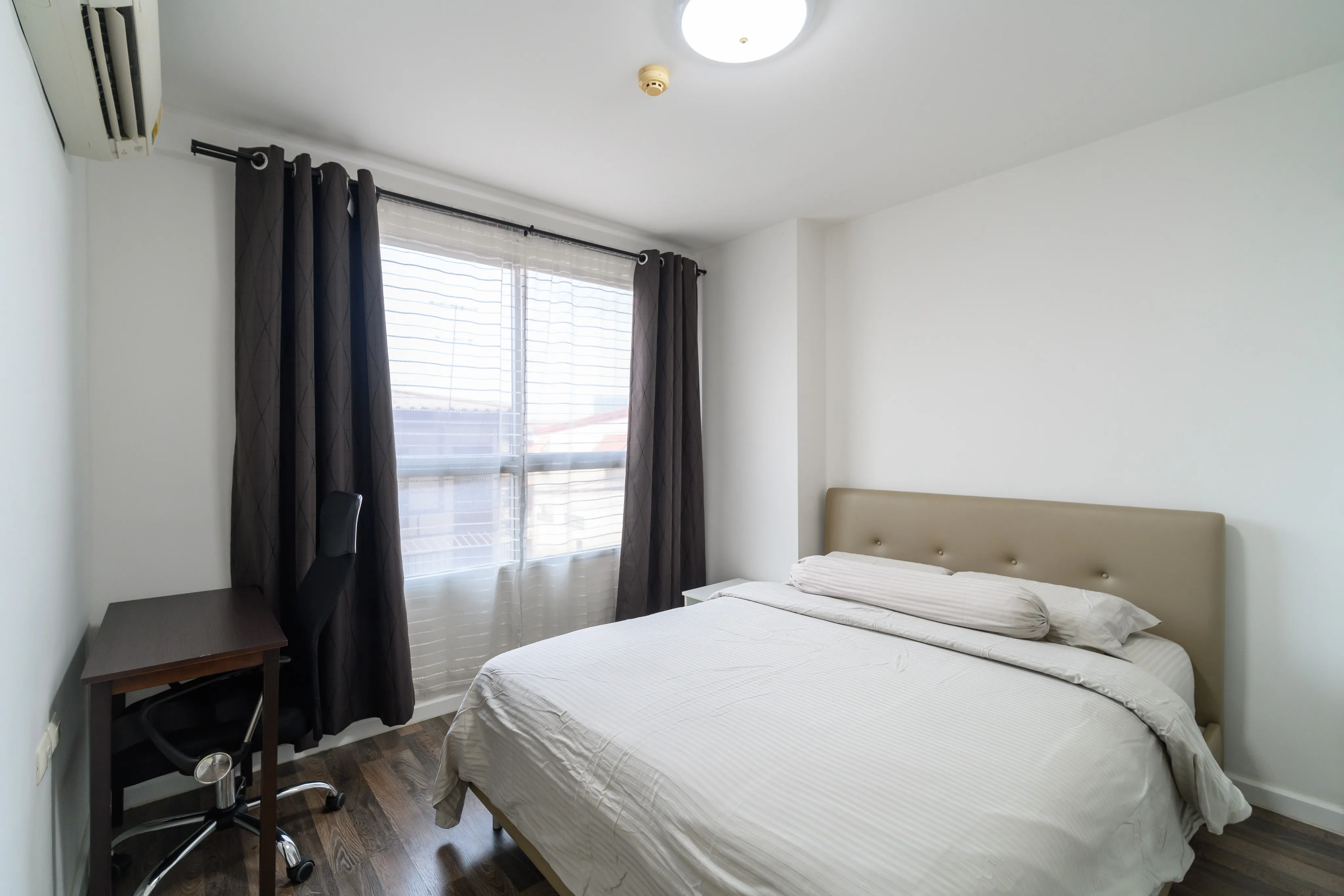 Compact white bedroom with a double bed, desk, and dark curtains
