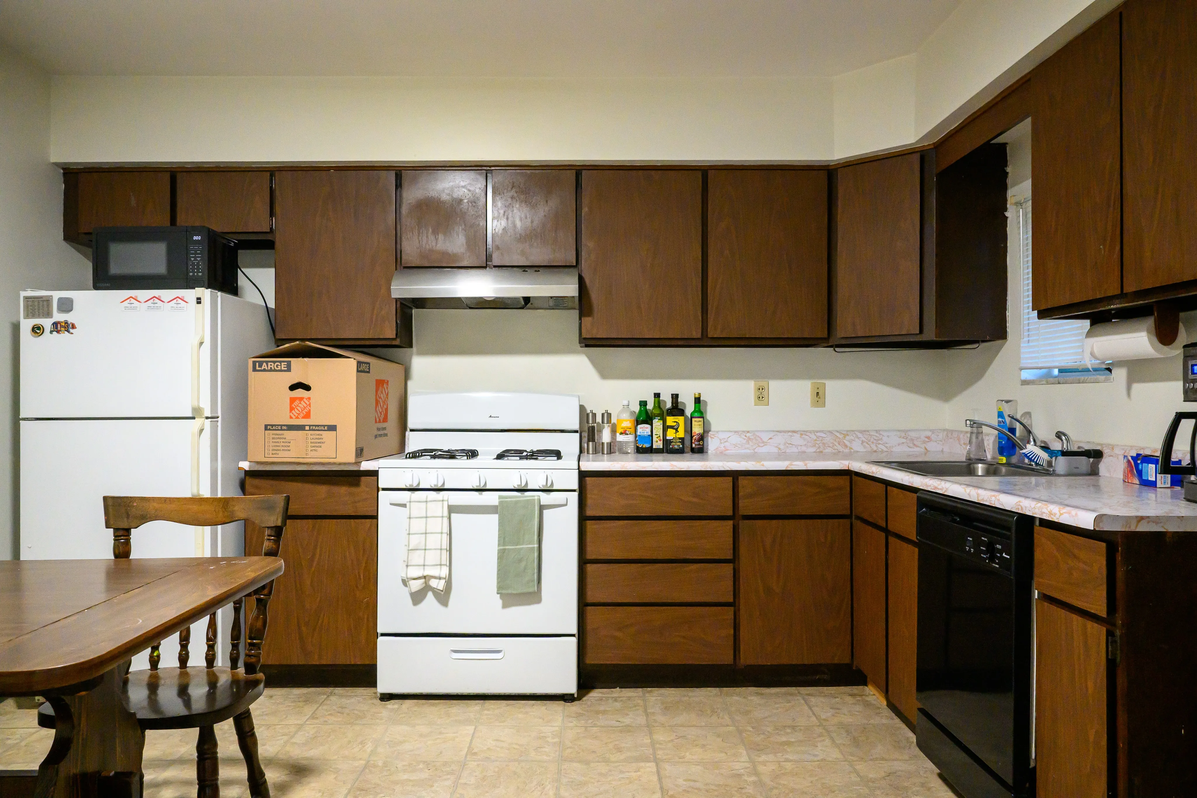 Apartment kitchen with dark wood cabinets, white appliances, and a small dining table
