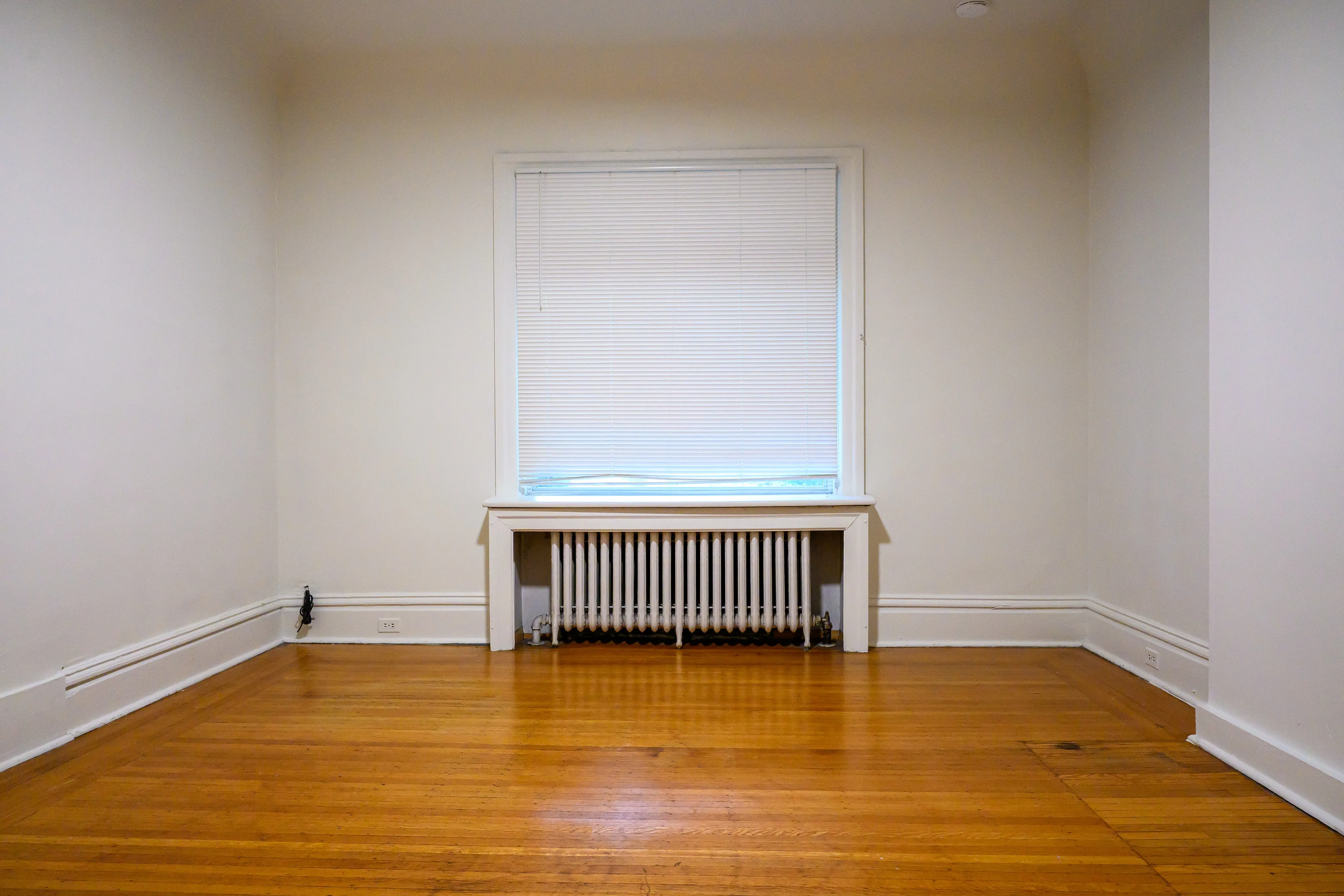 Empty room with hardwood flooring, a radiator, and a single shaded window