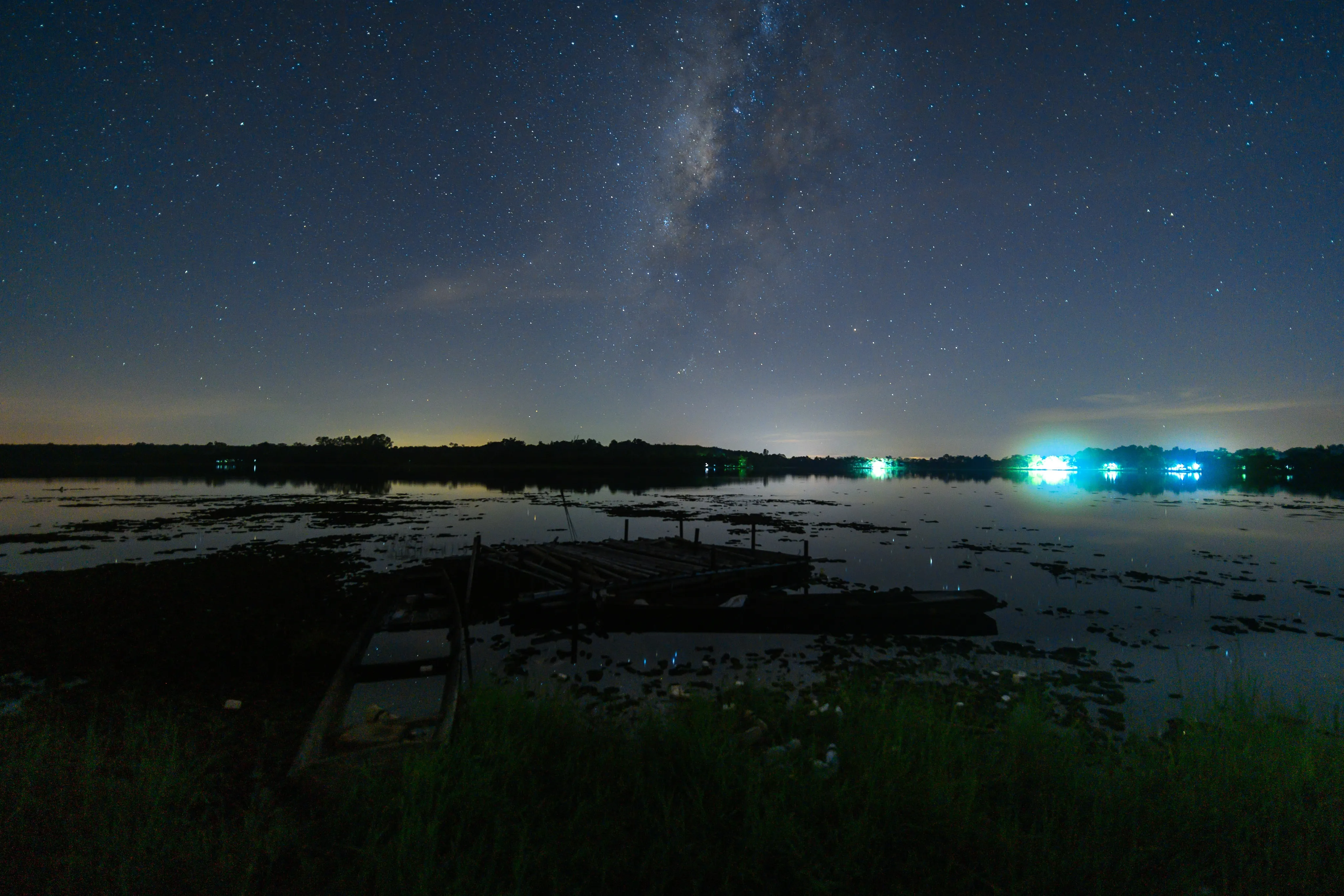 The Milky Way above a wetland with distant lights on the horizon