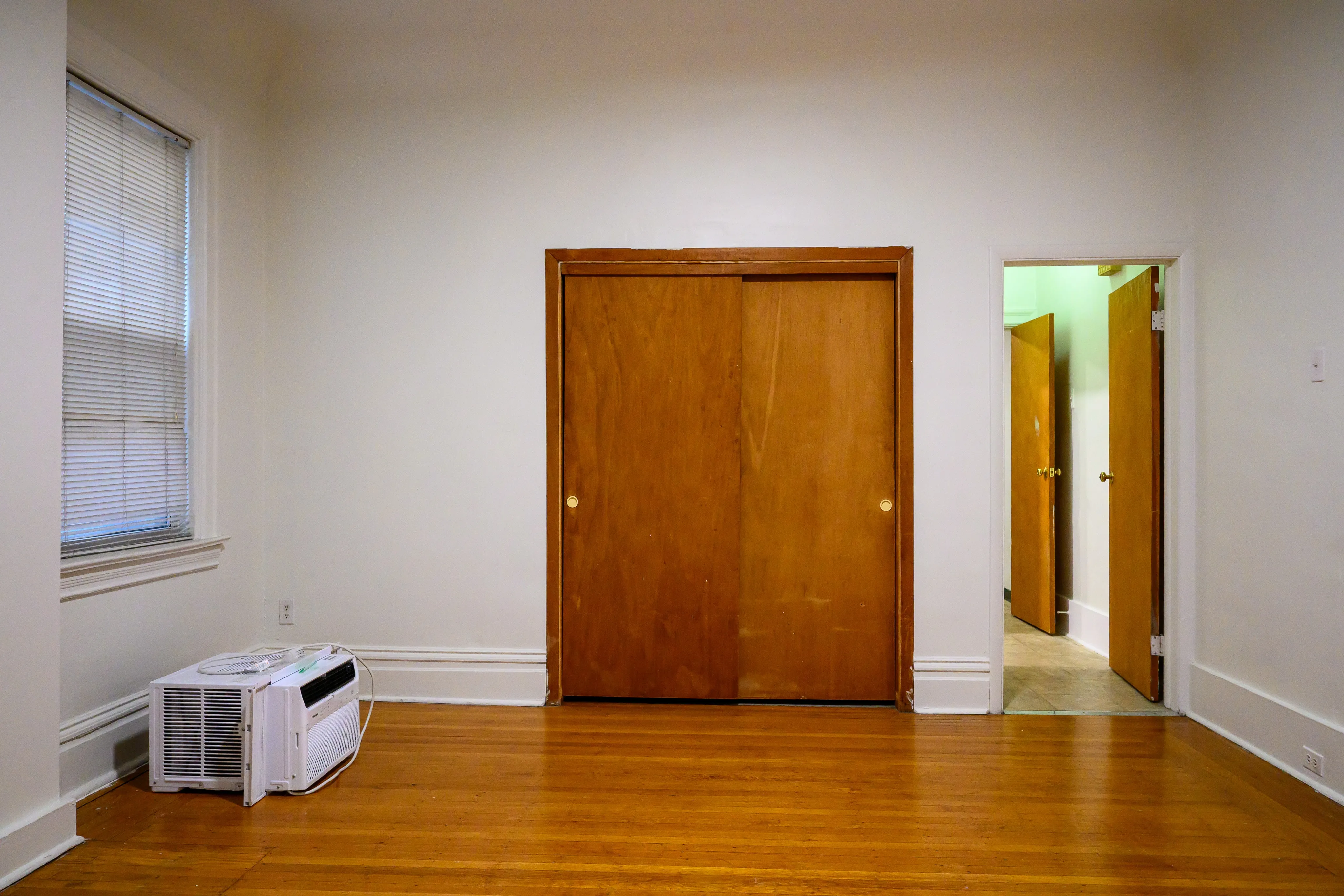 Empty hardwood room facing a closet and an illuminated hallway doorway