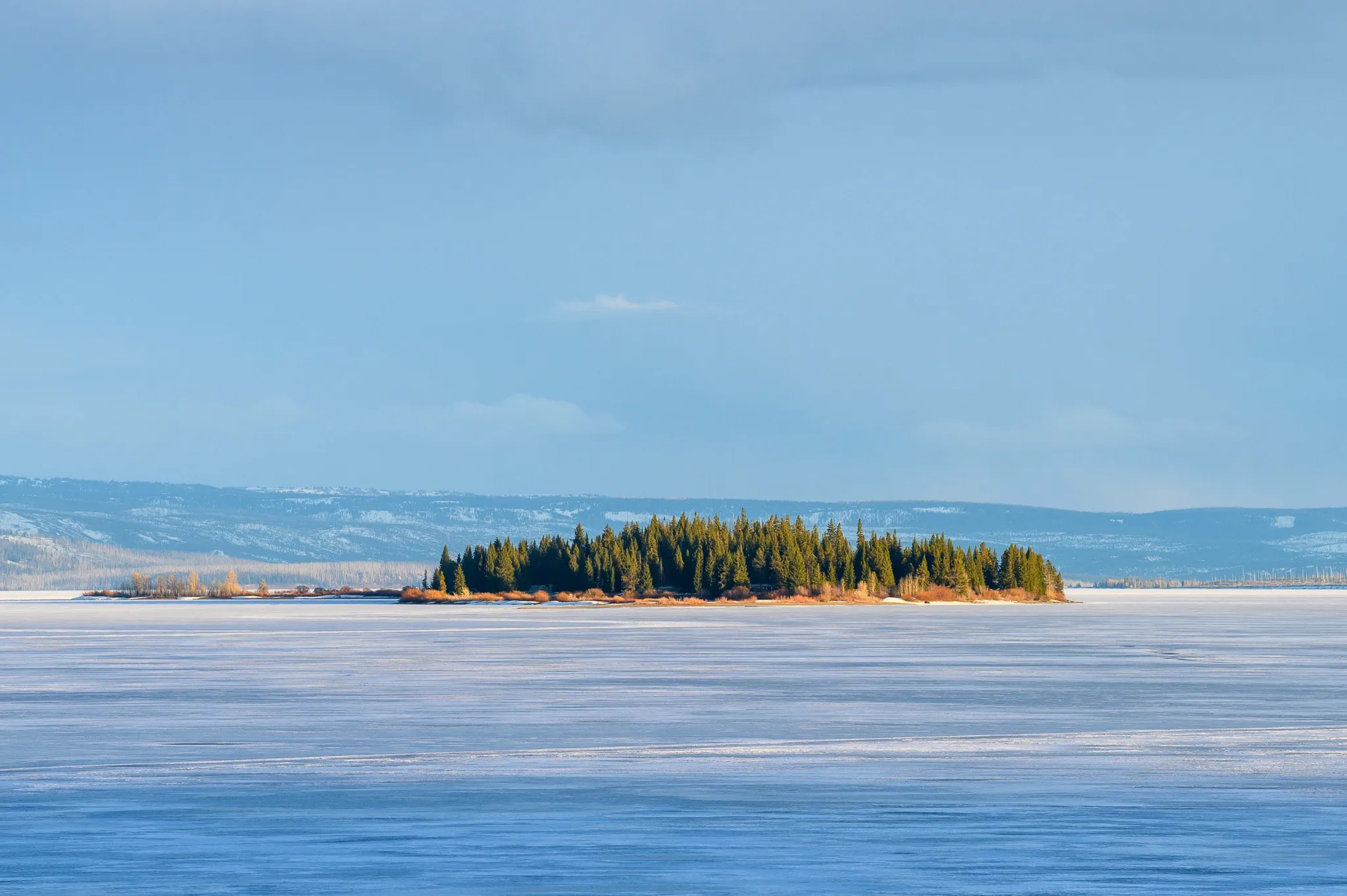 Small tree-covered island surrounded by a frozen blue lake