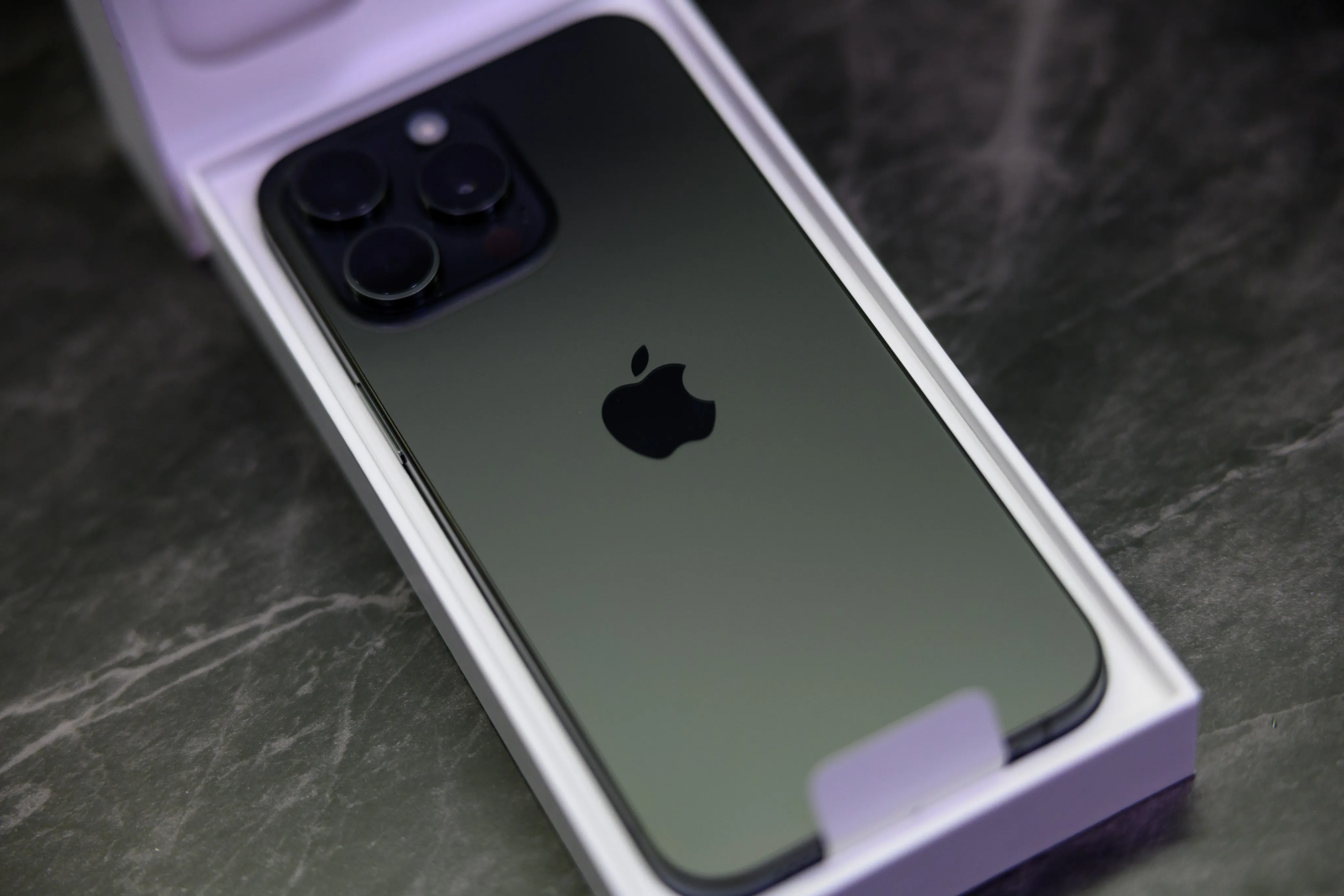A new iPhone lying in its open lavender box on a dark marble surface