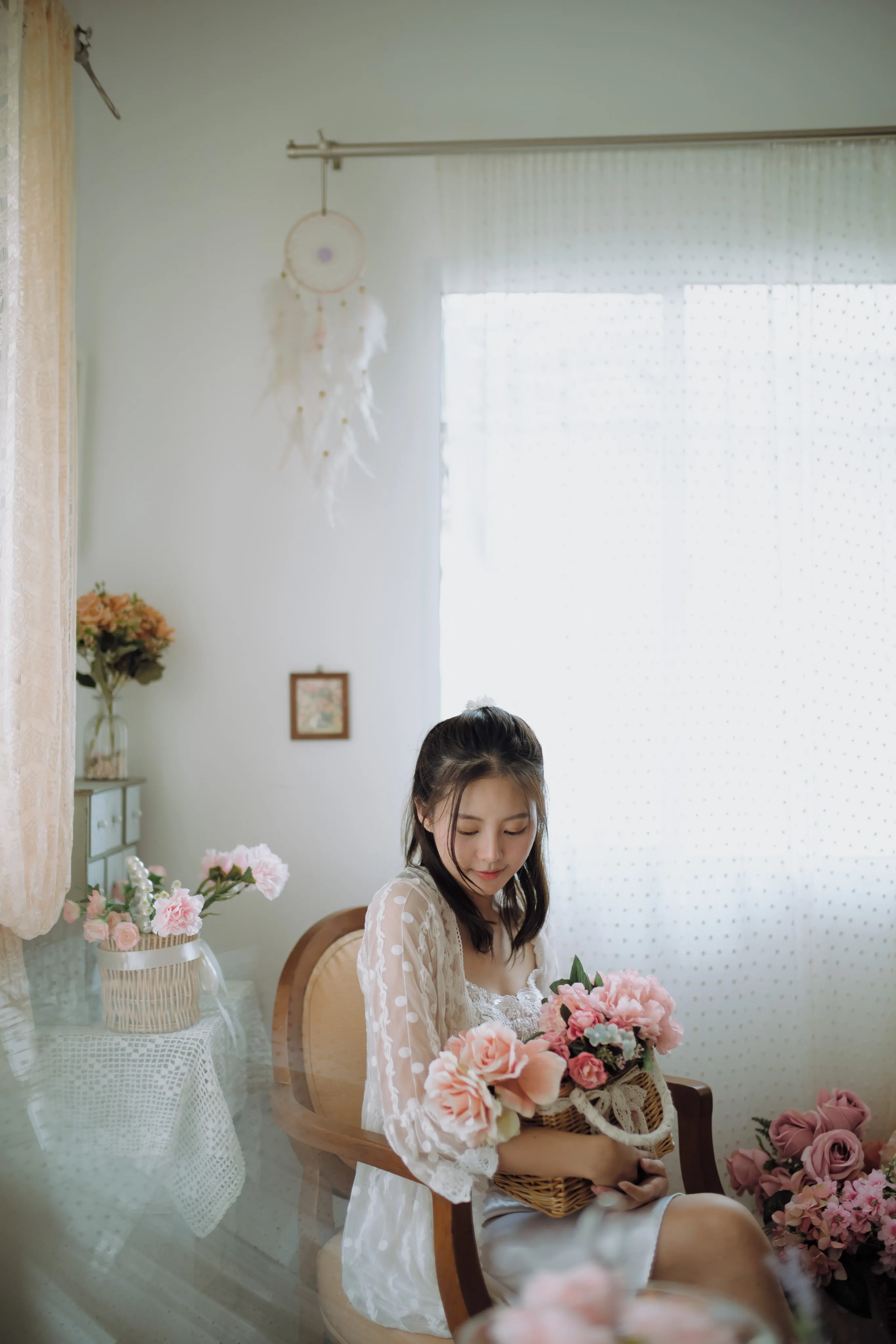 A woman in white lace seated with a bouquet in a bright, softly lit room.