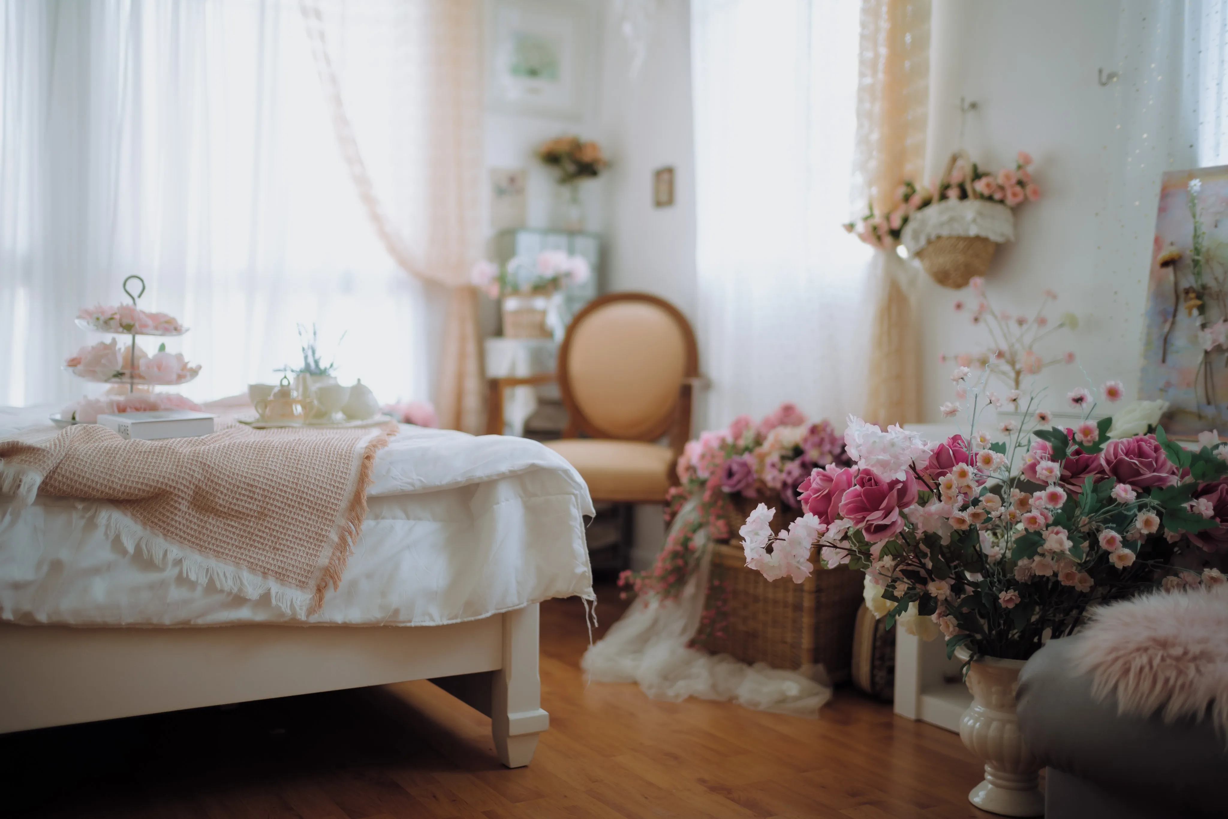 A bright bedroom still life of flowers and a tiered tea stand in soft window light.
