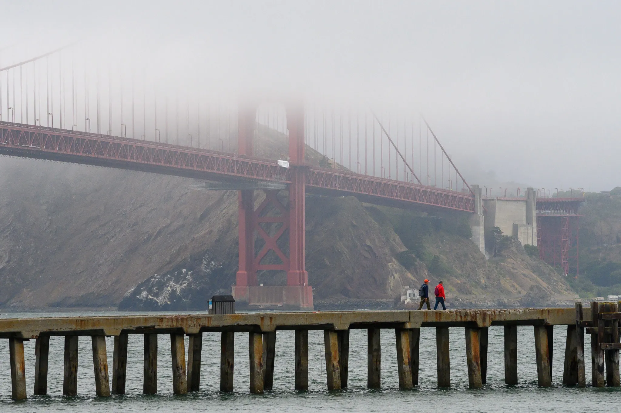 Golden Gate Bridge emerging through fog beyond a waterfront railing