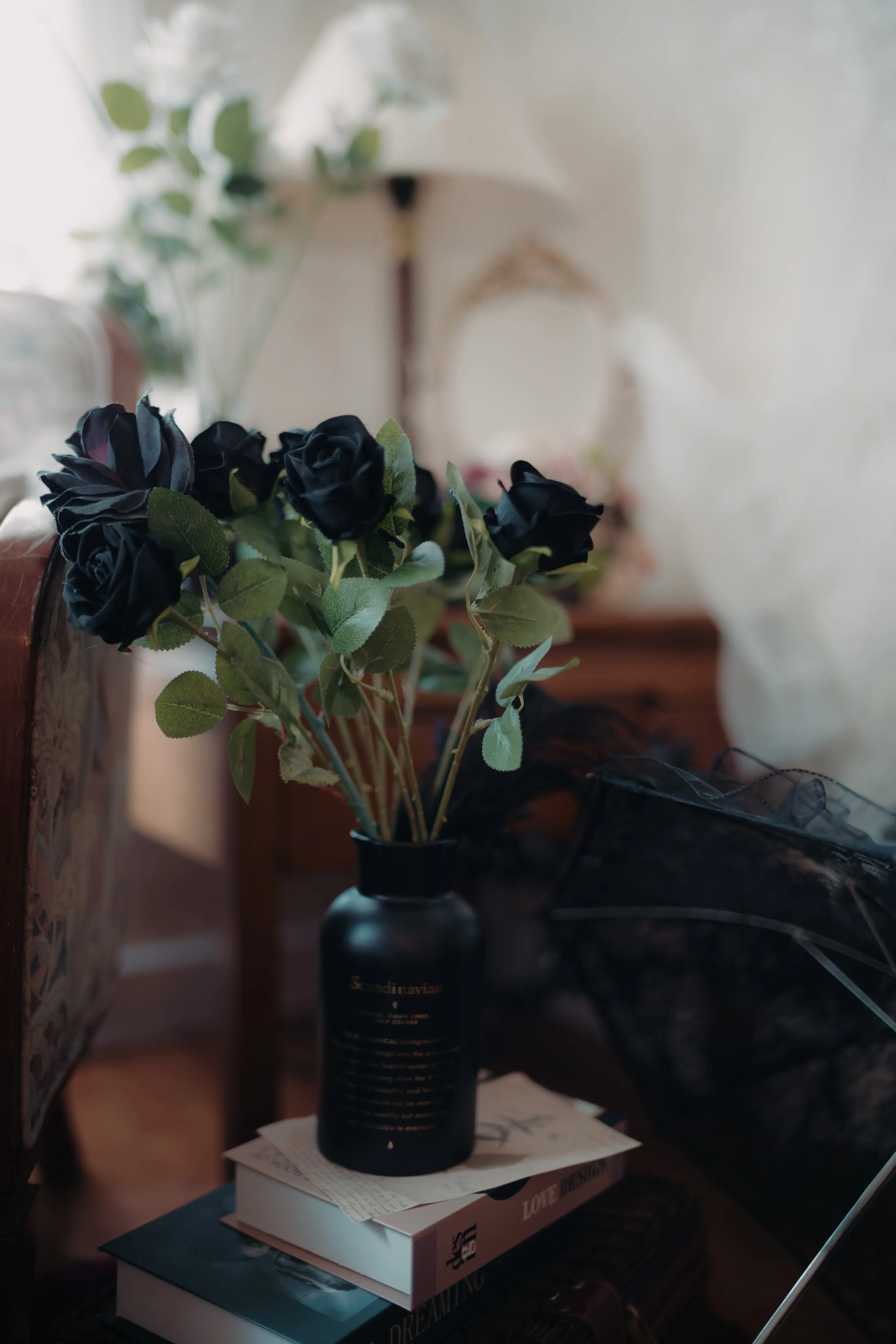 Black roses in a dark vase beside a lace umbrella and stacked books.