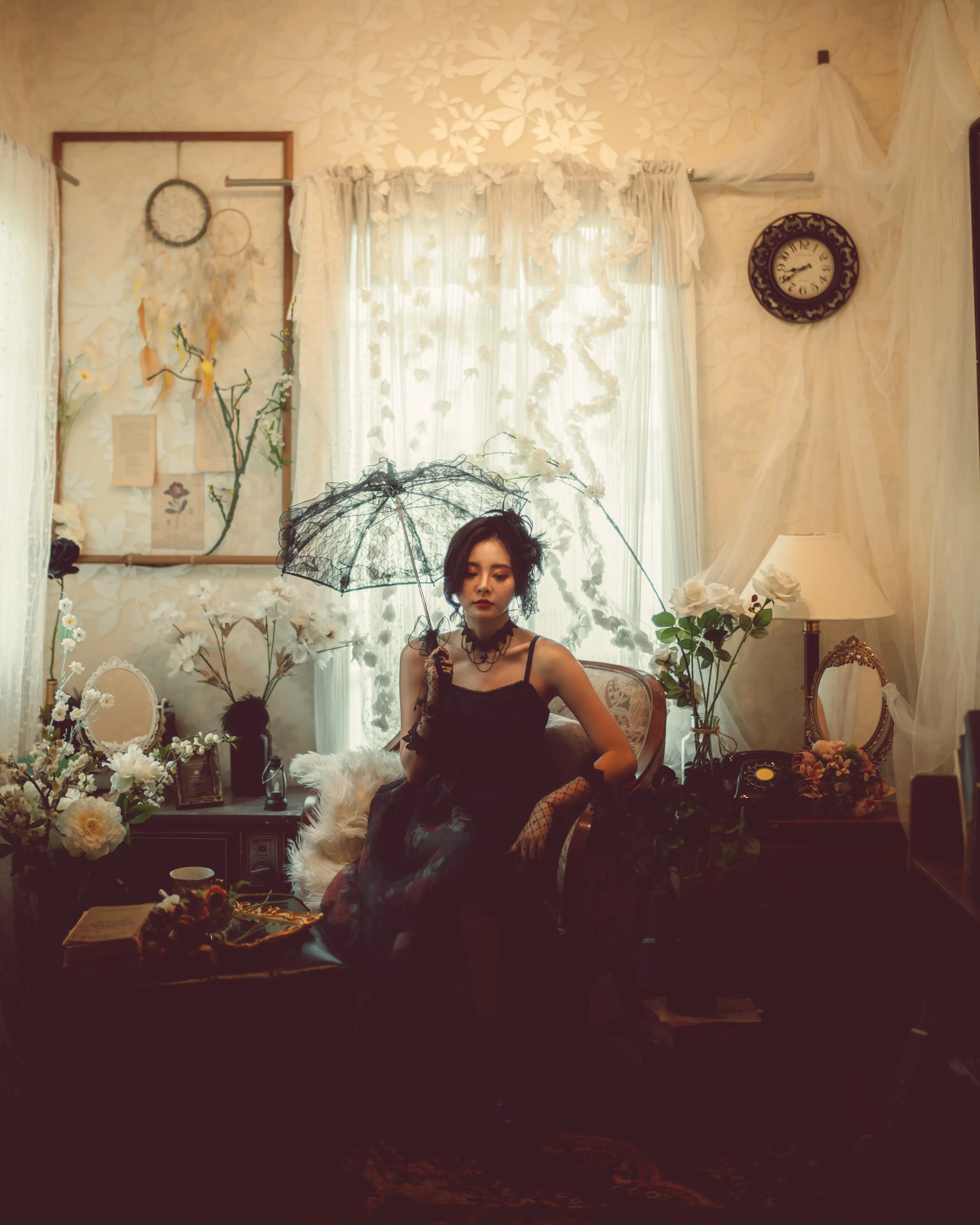 A woman in a black lace dress seated in a dim, shadowed room.
