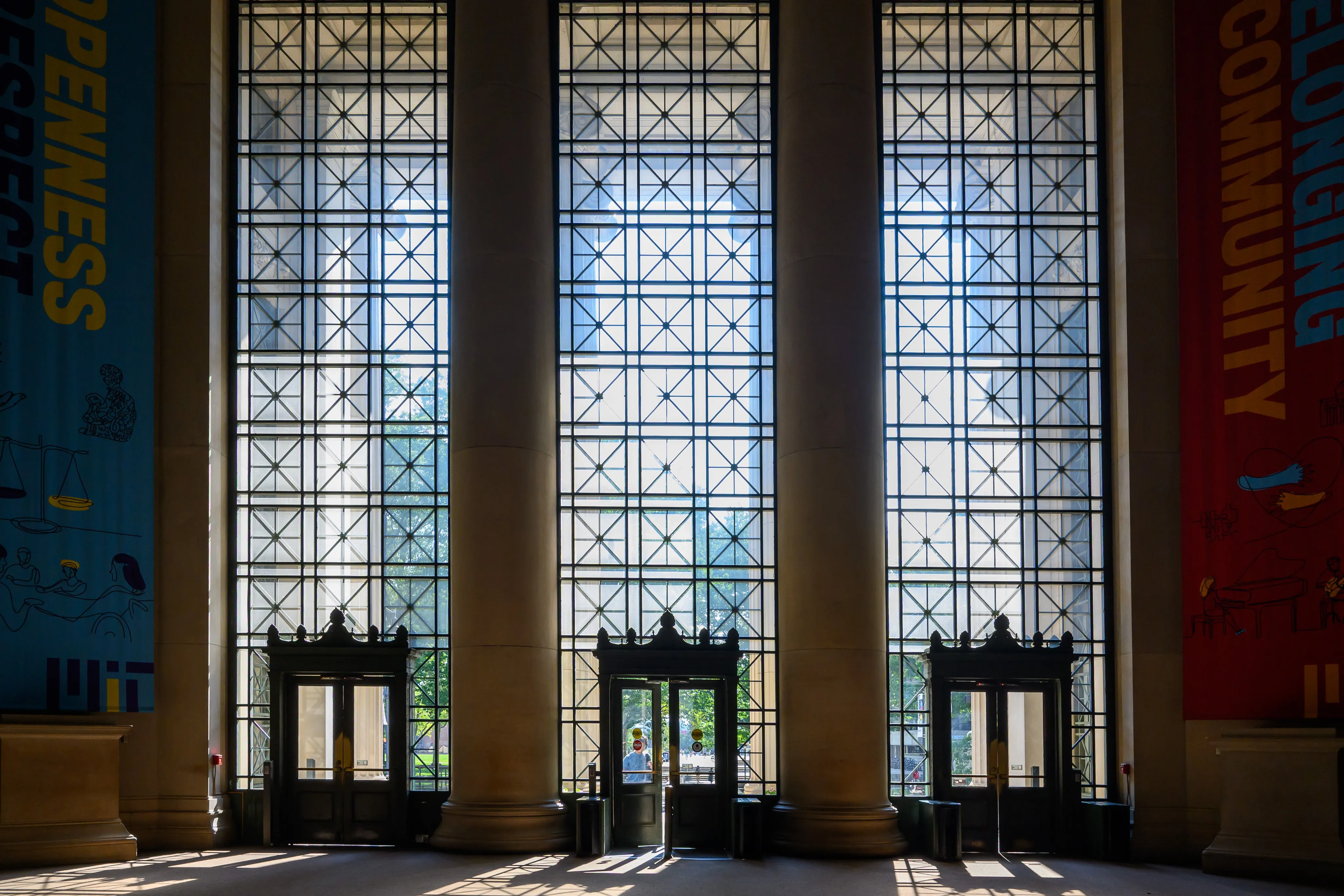 Tall gridded glass windows between stone columns above a row of doors in a grand hall