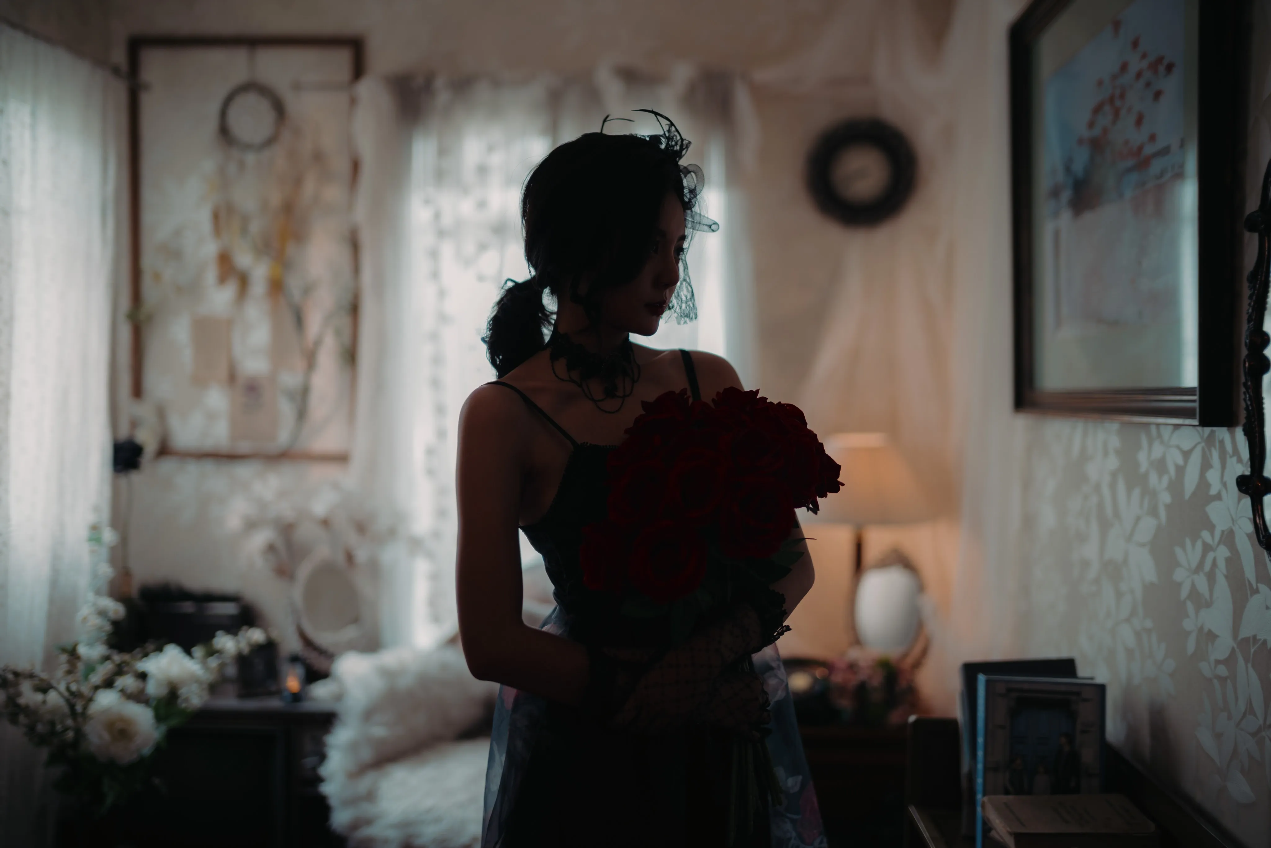 A woman in a black dress holding red roses, seen from behind in a dim room.