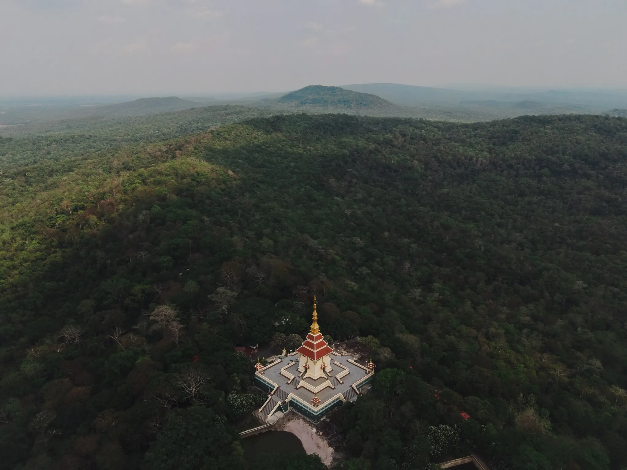 An aerial view of a gilded temple spire rising from forested hills