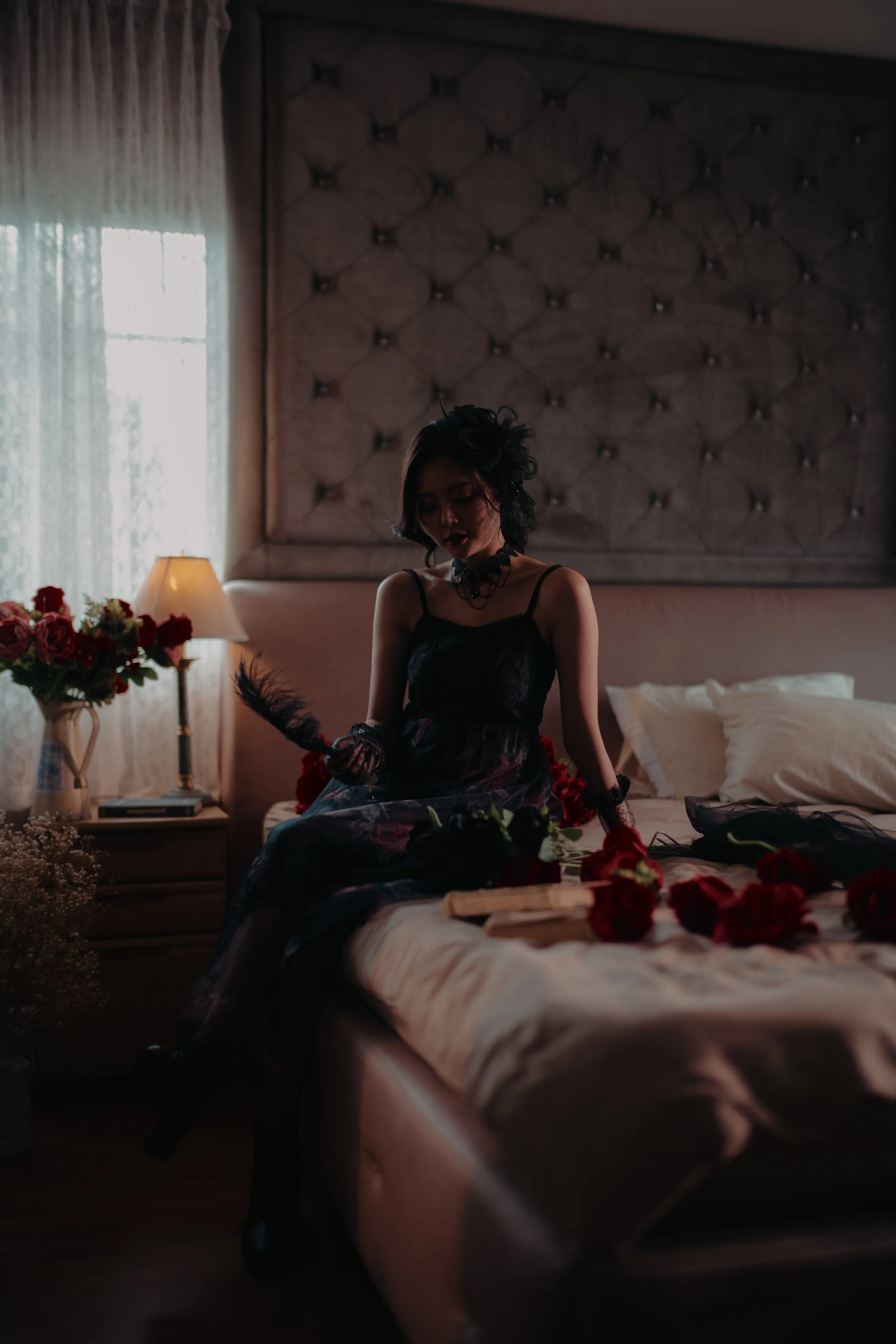 A woman in a black dress seated on a bed scattered with red roses.