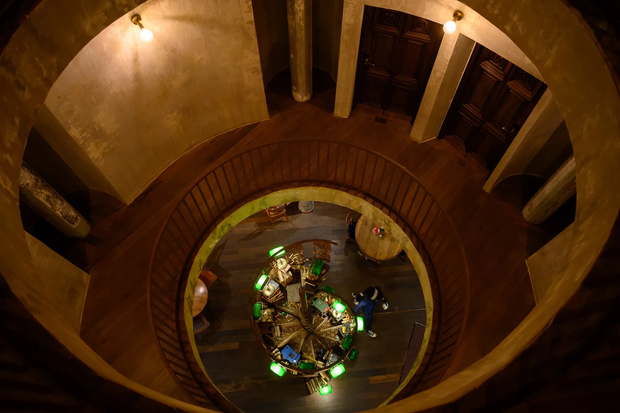 Looking down through a circular wooden stairwell to a green-lit chandelier below