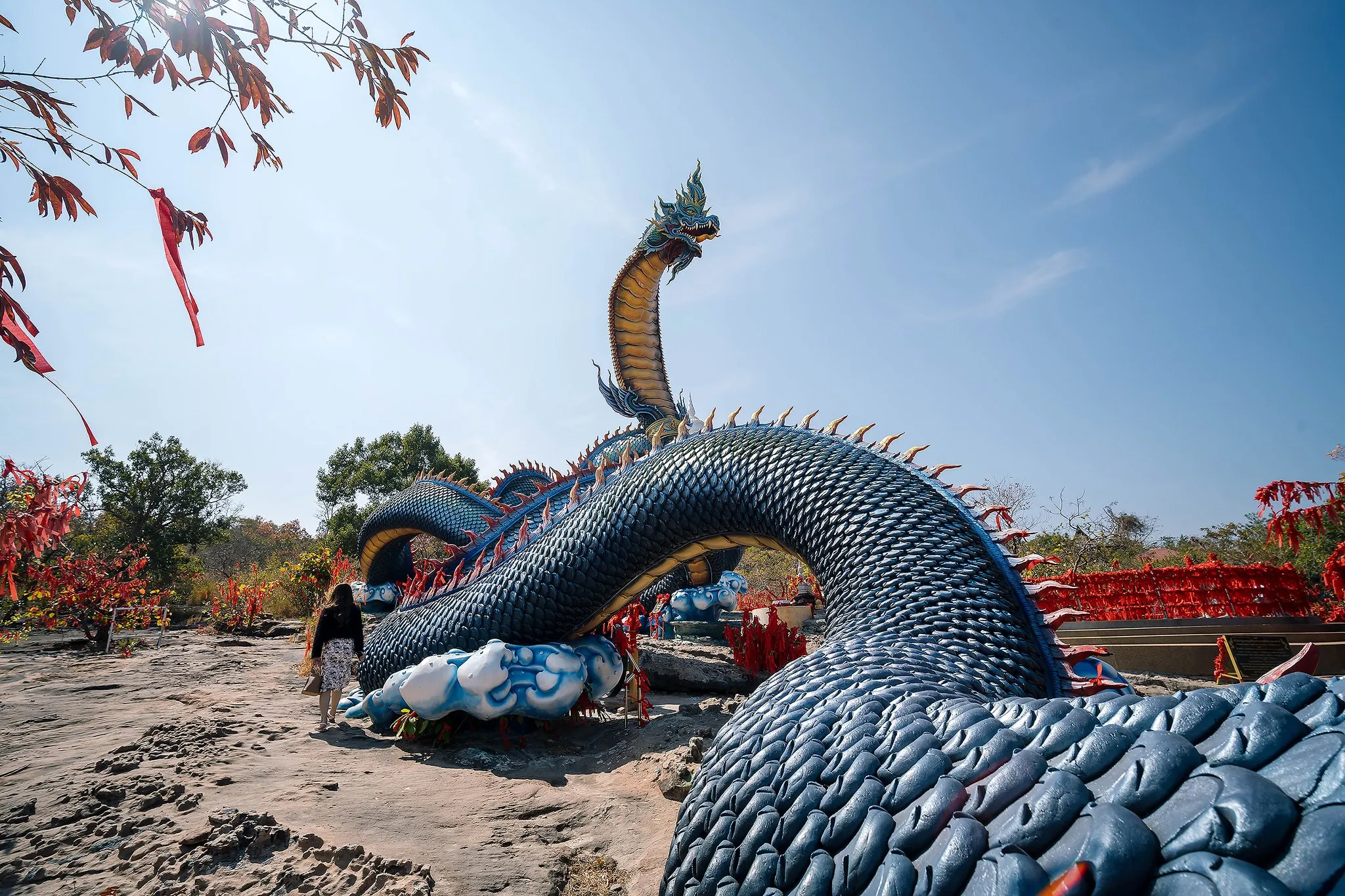 A giant blue naga serpent sculpture coiling across a rocky hilltop under a blue sky