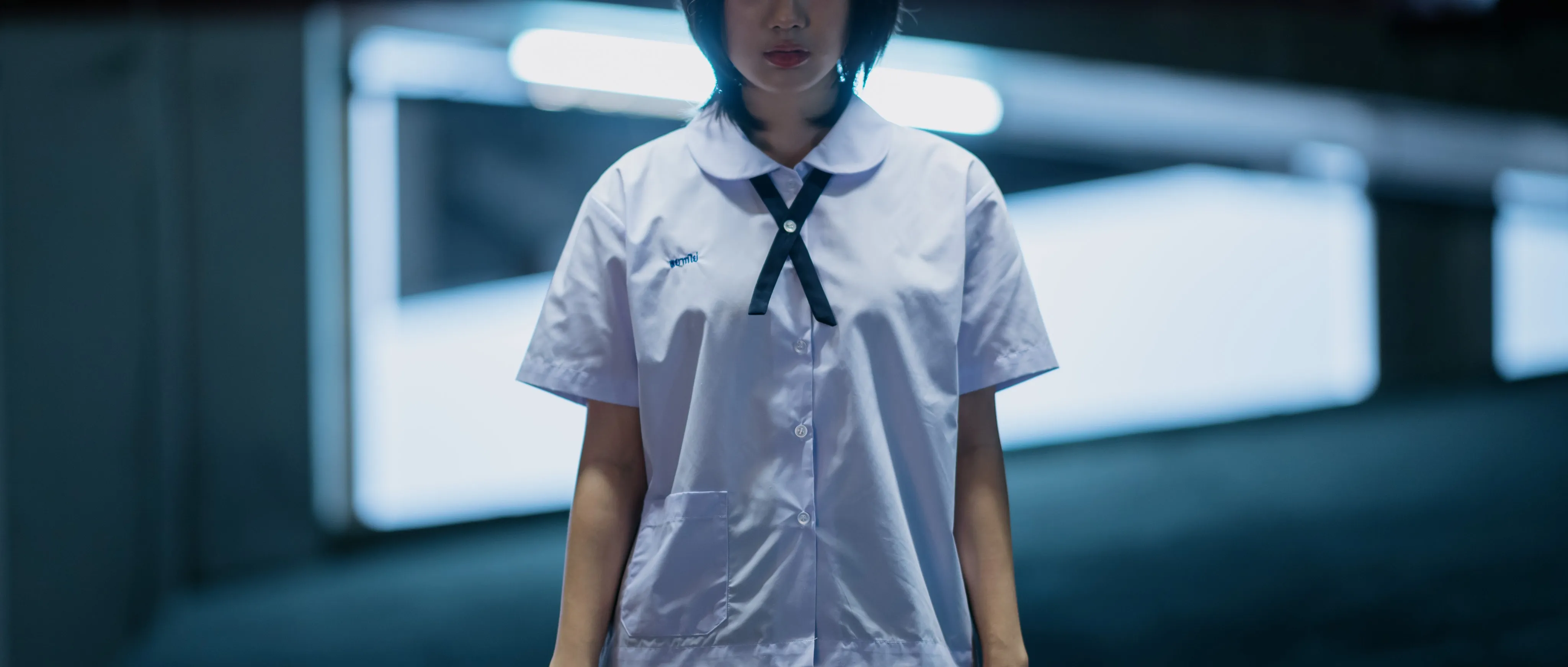 A girl in a school uniform standing expressionless in a parking garage.