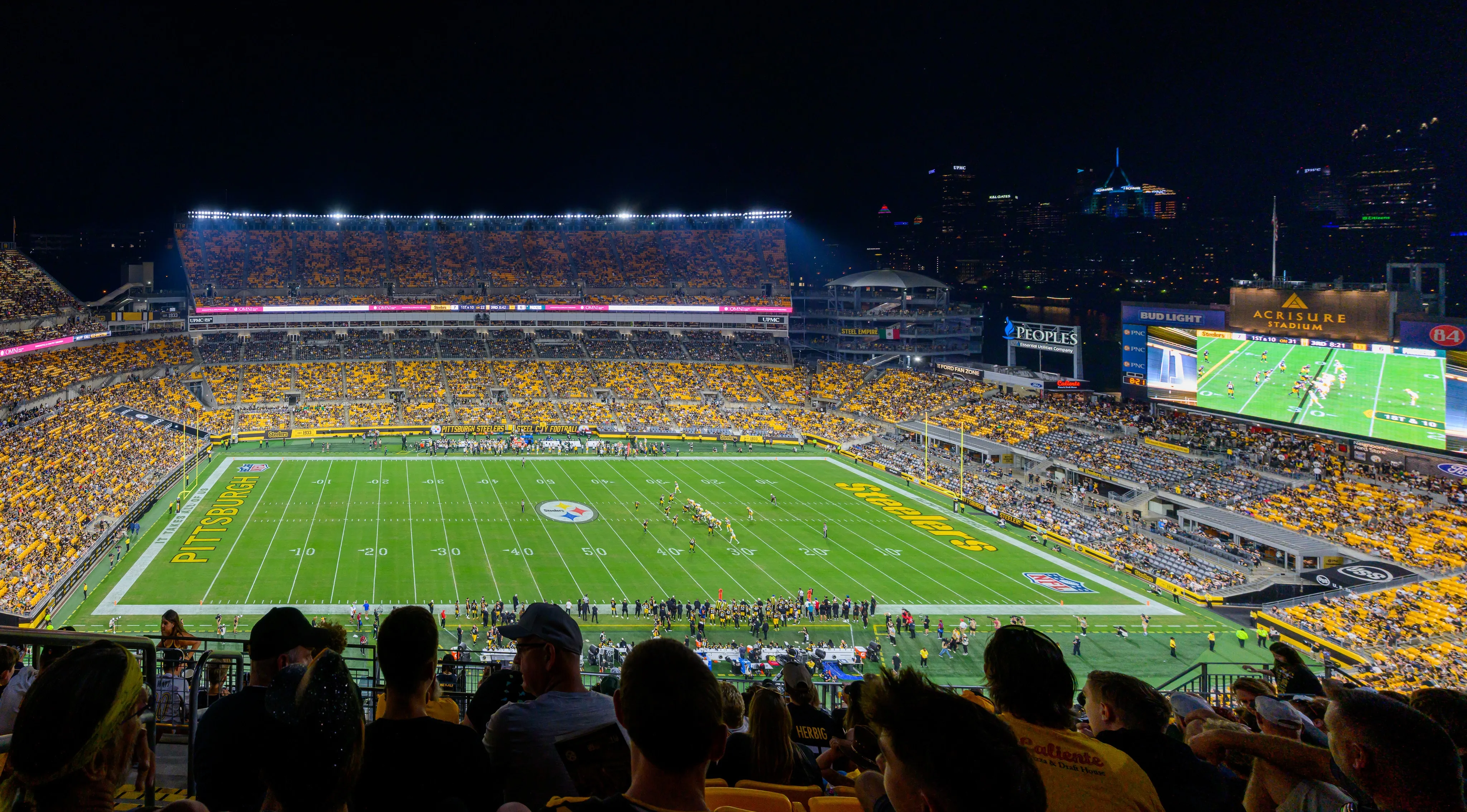 A football game at Acrisure Stadium with Pittsburgh's downtown skyline beyond the stands