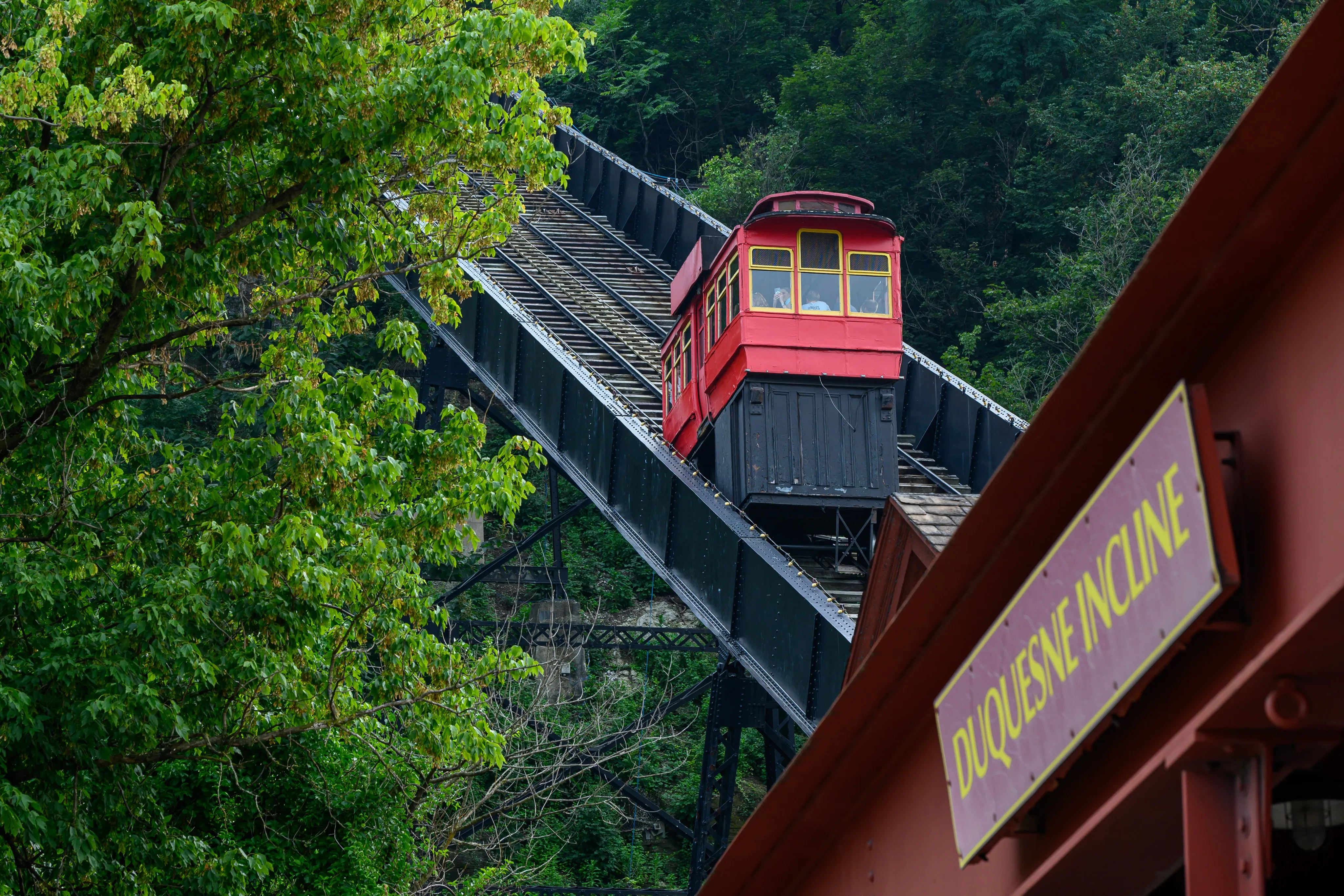 A red Duquesne Incline car climbing its hillside railway through green woodland