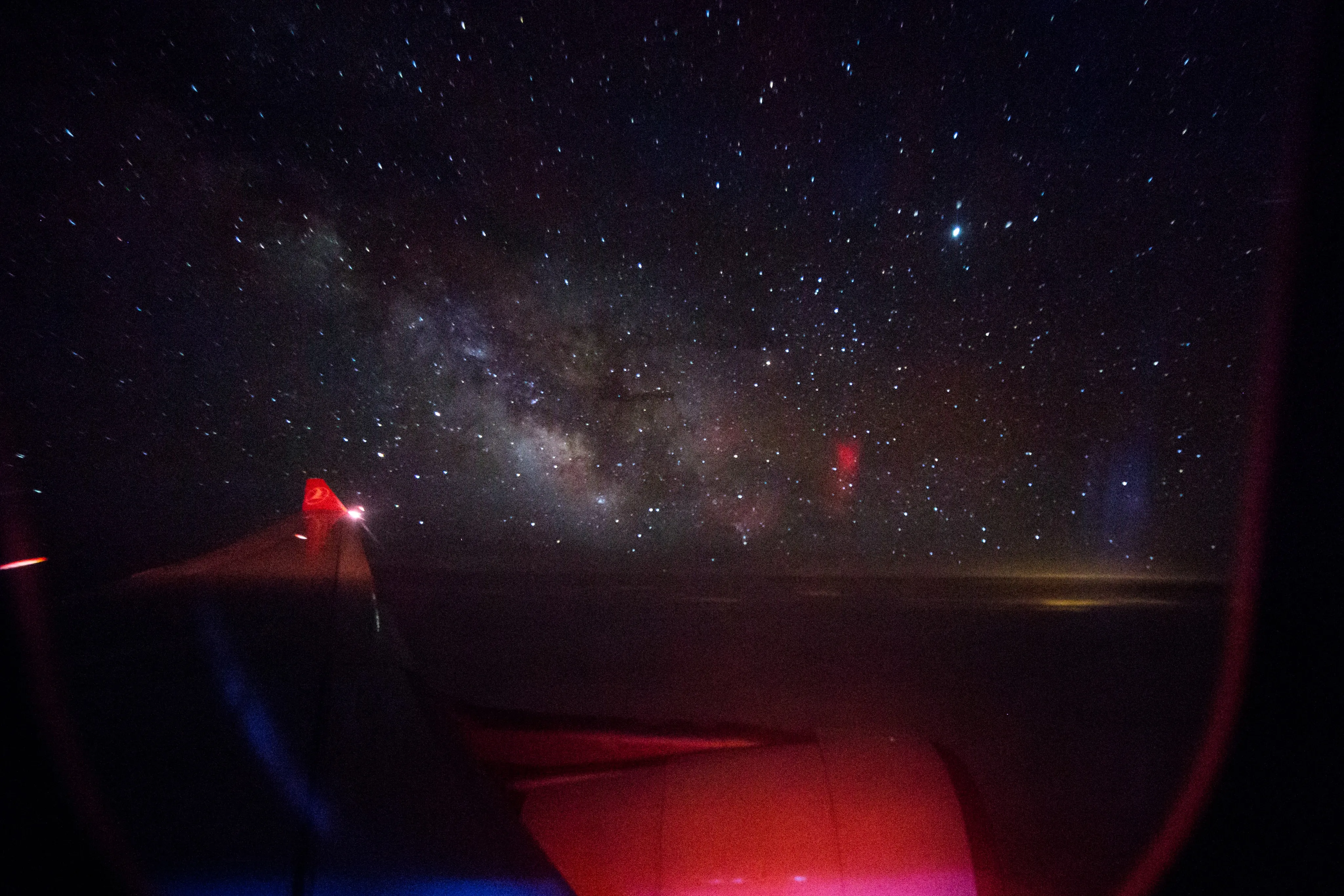 The Milky Way seen through an aircraft window above a red-lit wing