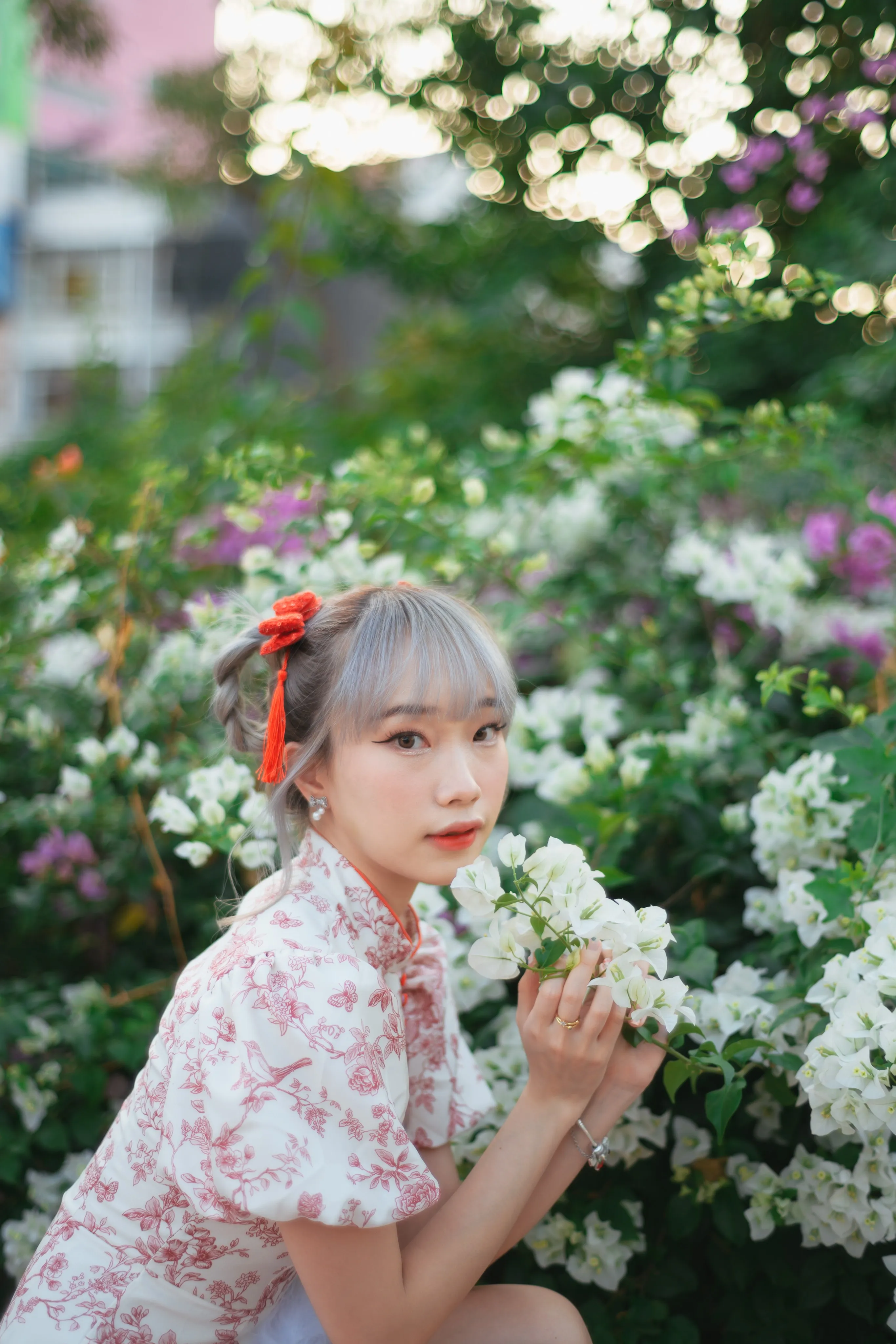 A woman in a floral cheongsam-style dress and a red hair ribbon holding white bougainvillea blossoms