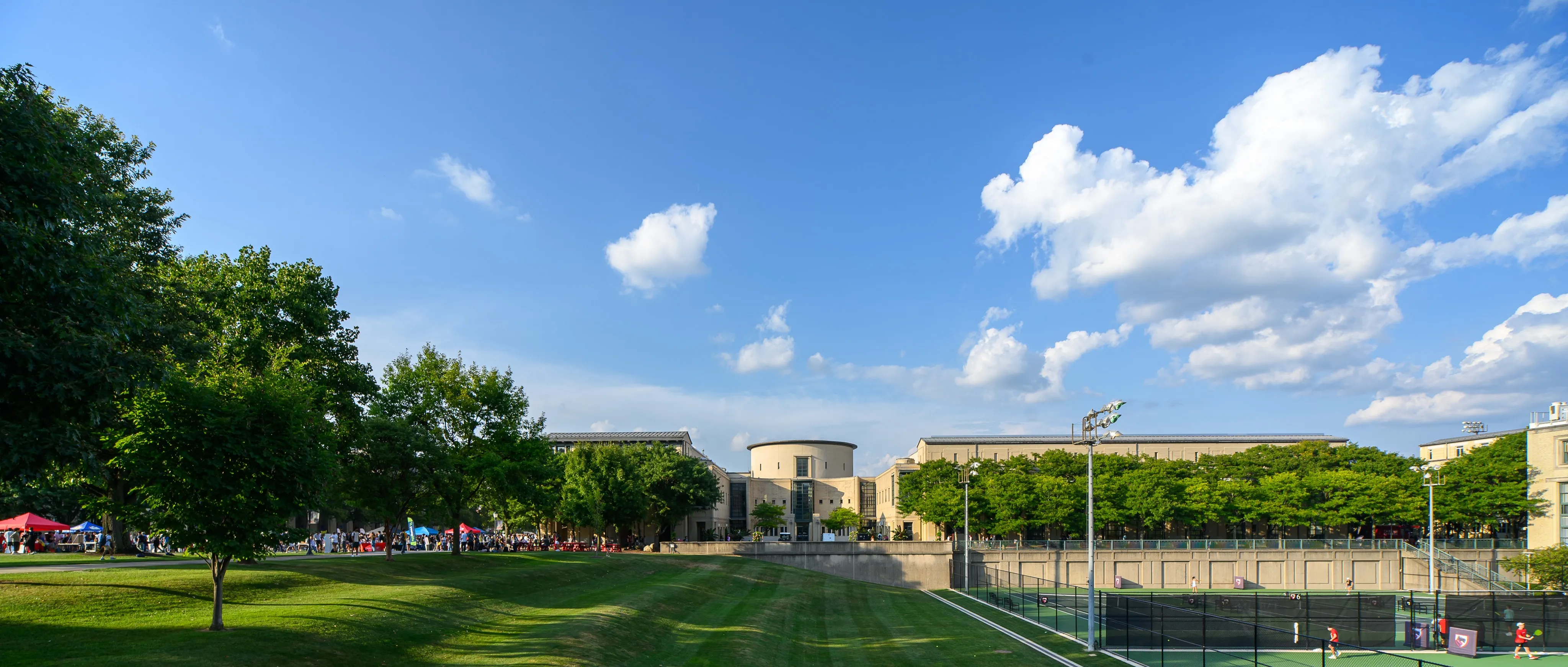 A sunny Carnegie Mellon University campus lawn and tennis courts beneath a bright blue sky