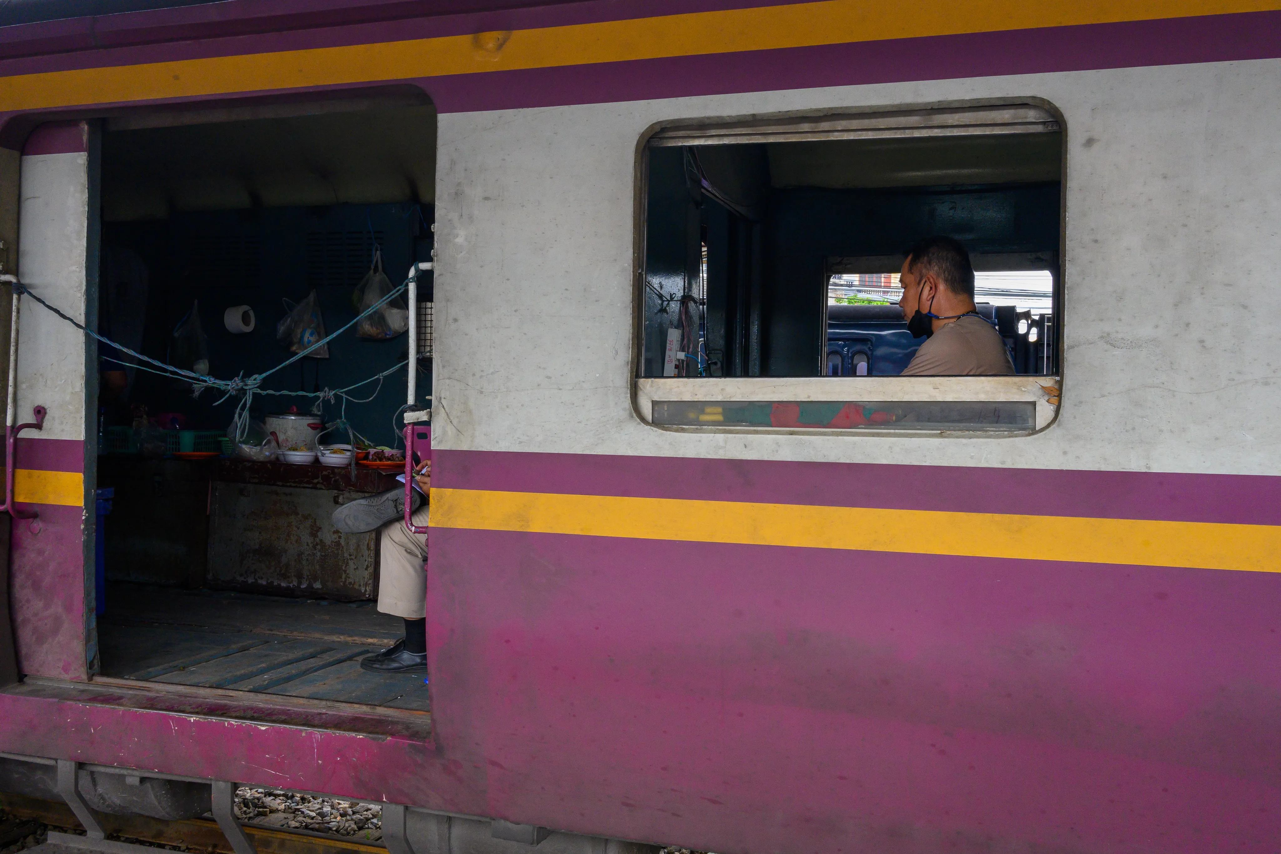 Passenger seen through the open window of a purple-and-cream train