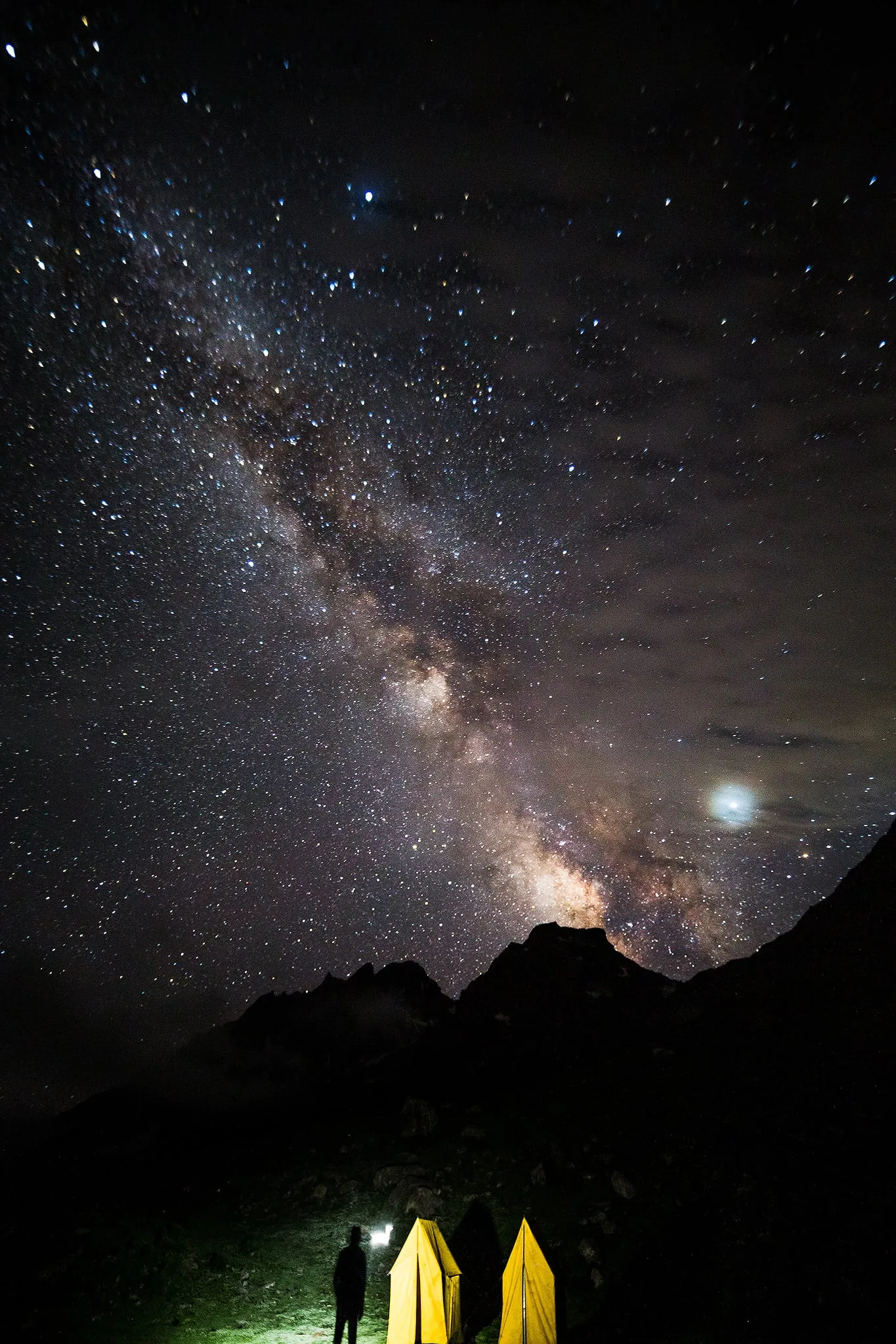 The Milky Way above mountains and two illuminated tents
