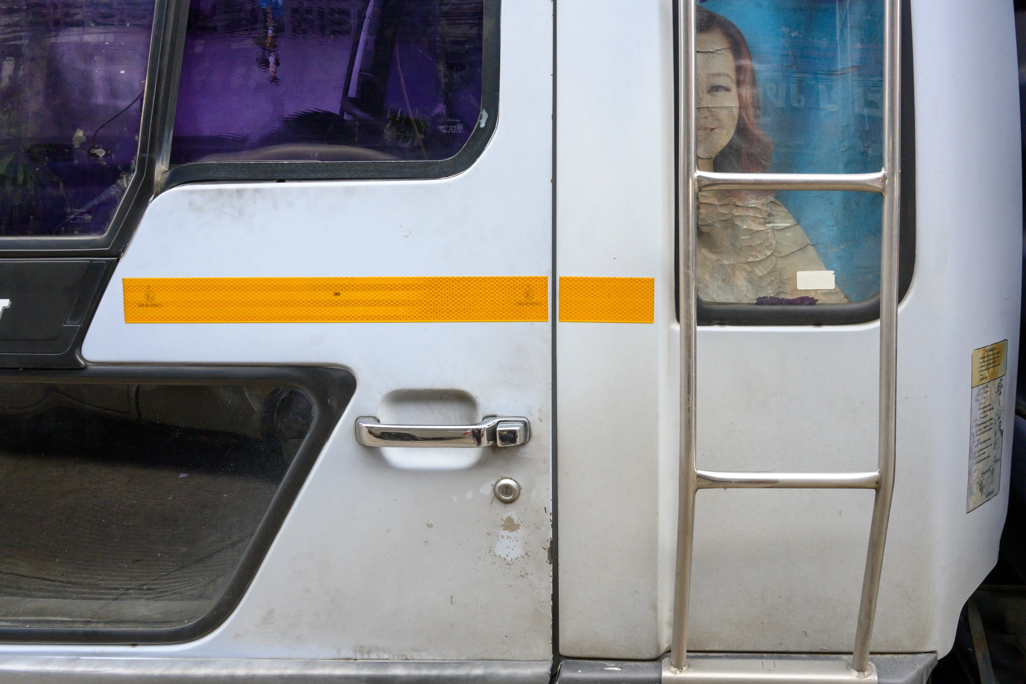 A white truck door with an orange stripe, a portrait poster visible through its window
