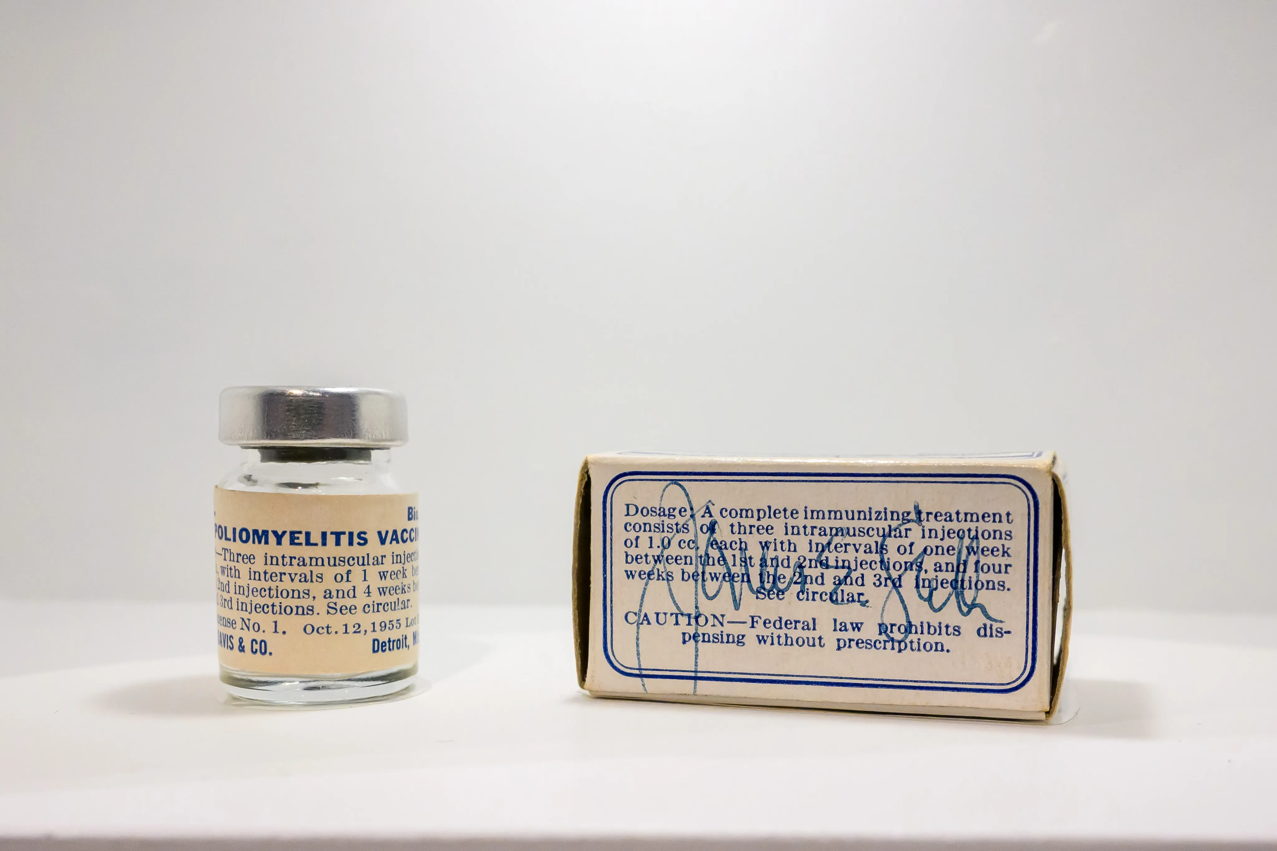 A small glass bottle beside its printed carton